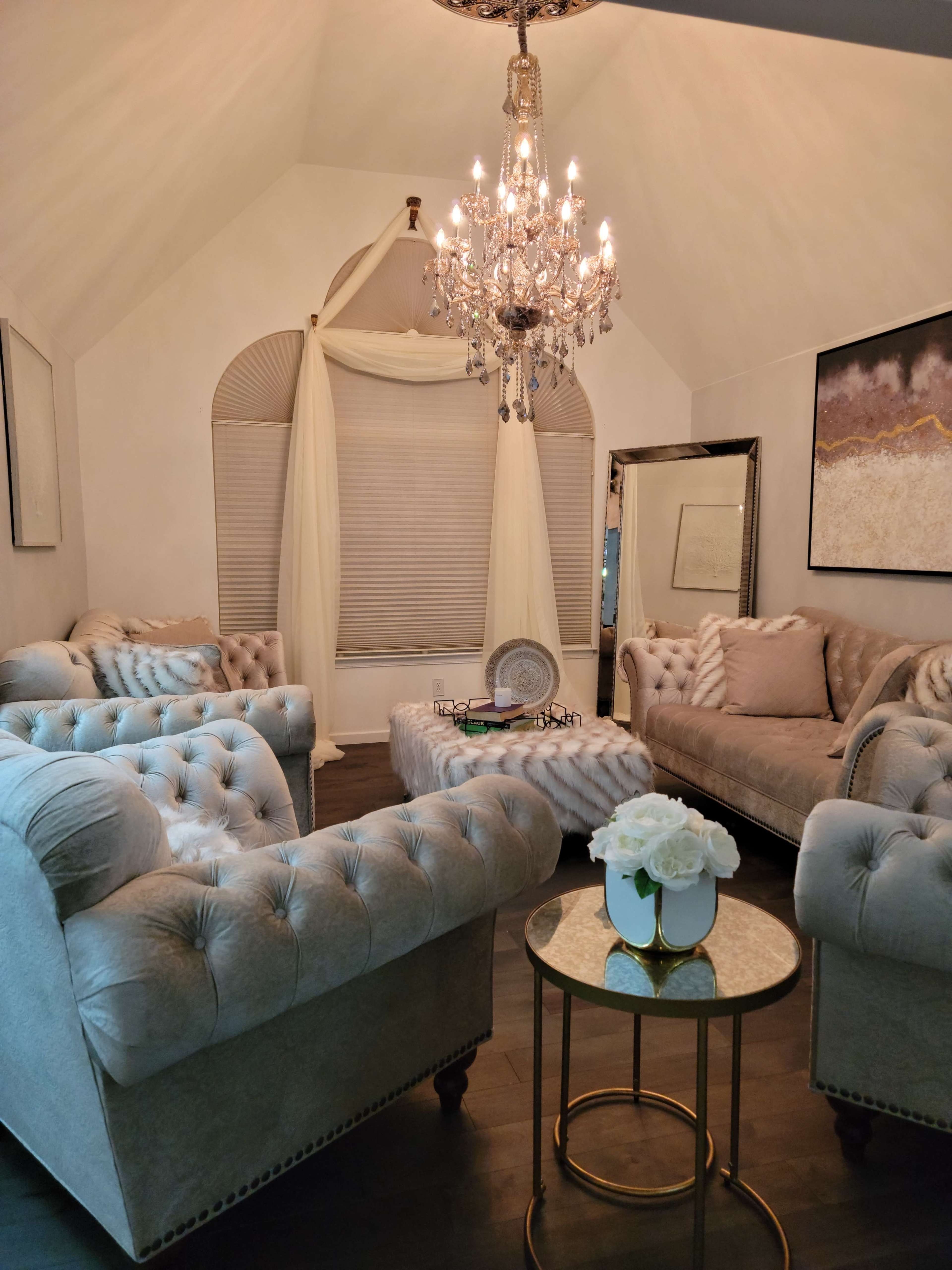 A stylish living room with tufted gray sofas, a round coffee table, and a chandelier hanging from a vaulted ceiling.