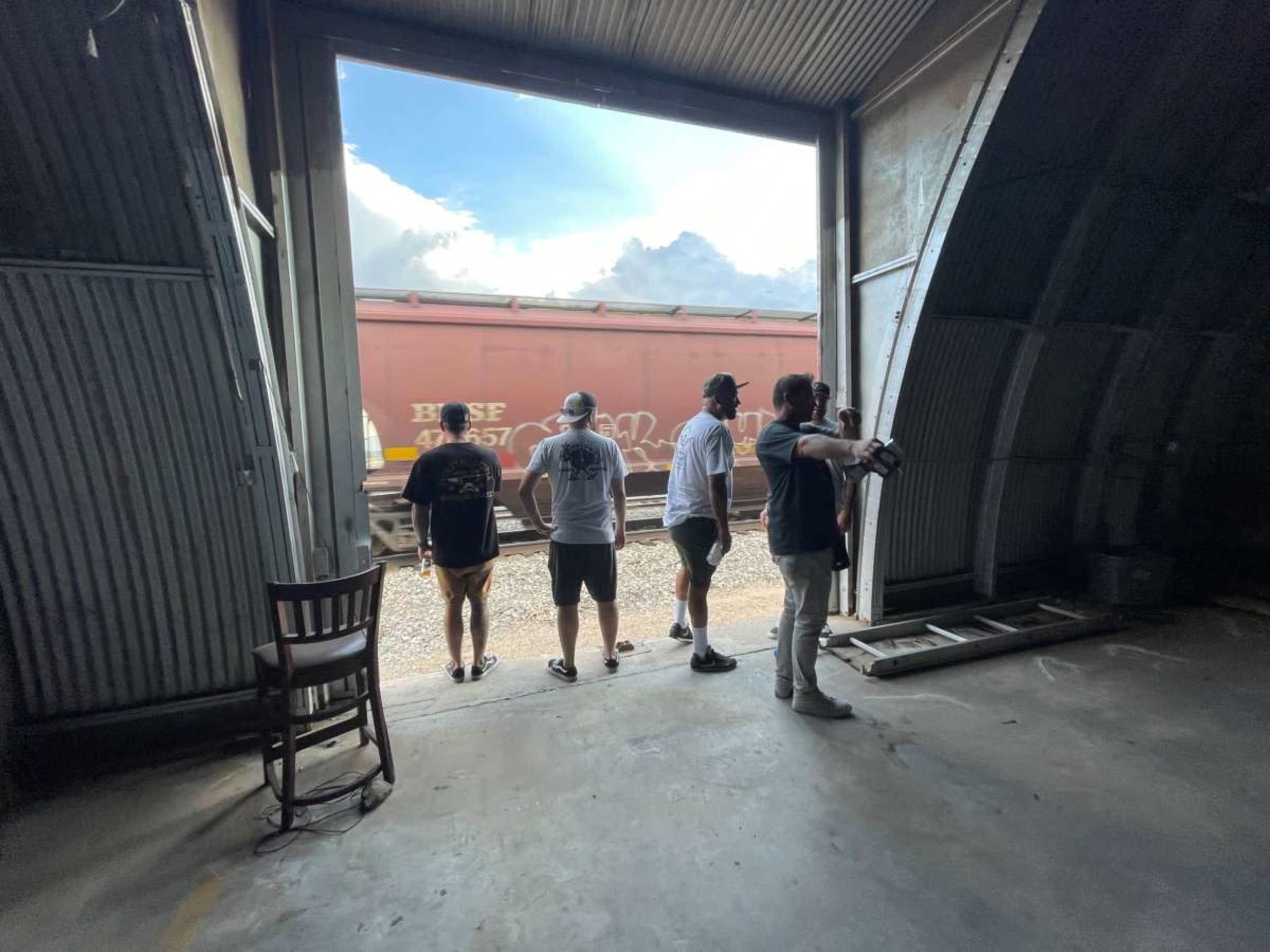 Four individuals stand in a doorway of a building, watching a passing train outside.