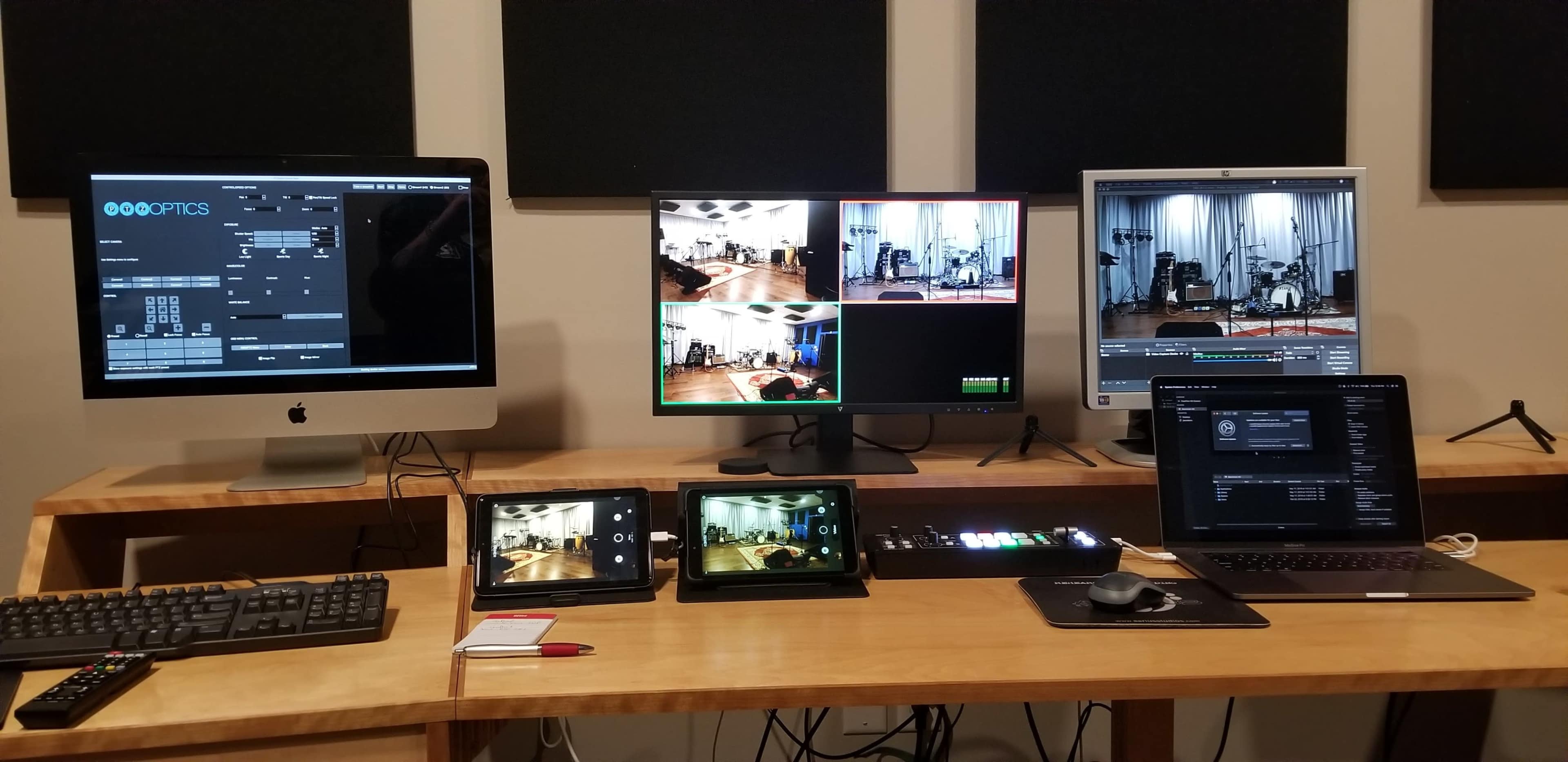A multimedia setup with multiple screens and devices displaying a live video feed and control interface, arranged on a wooden desk.