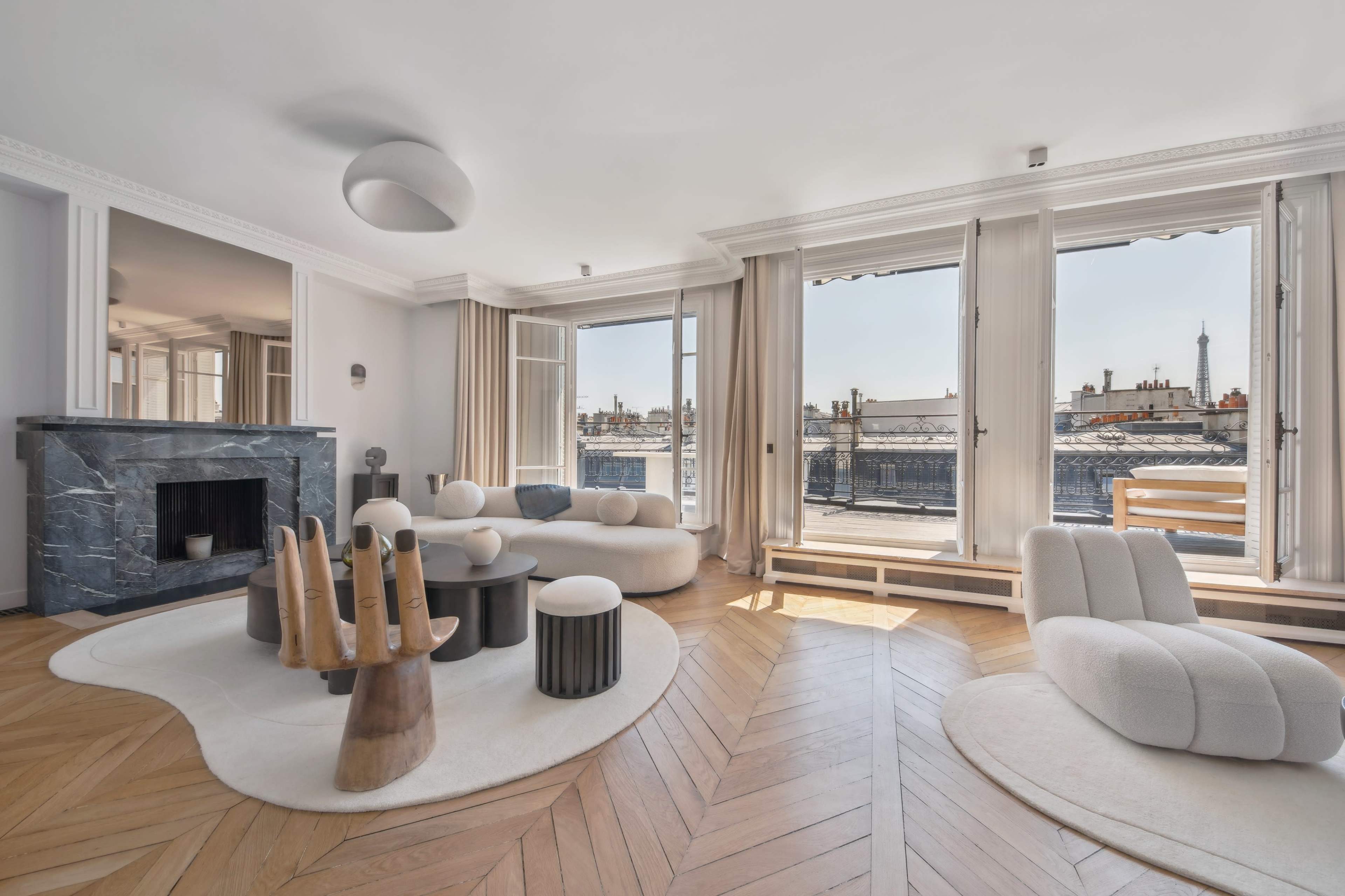 The spacious living room features a marble fireplace, modern furniture, and large windows overlooking a cityscape.