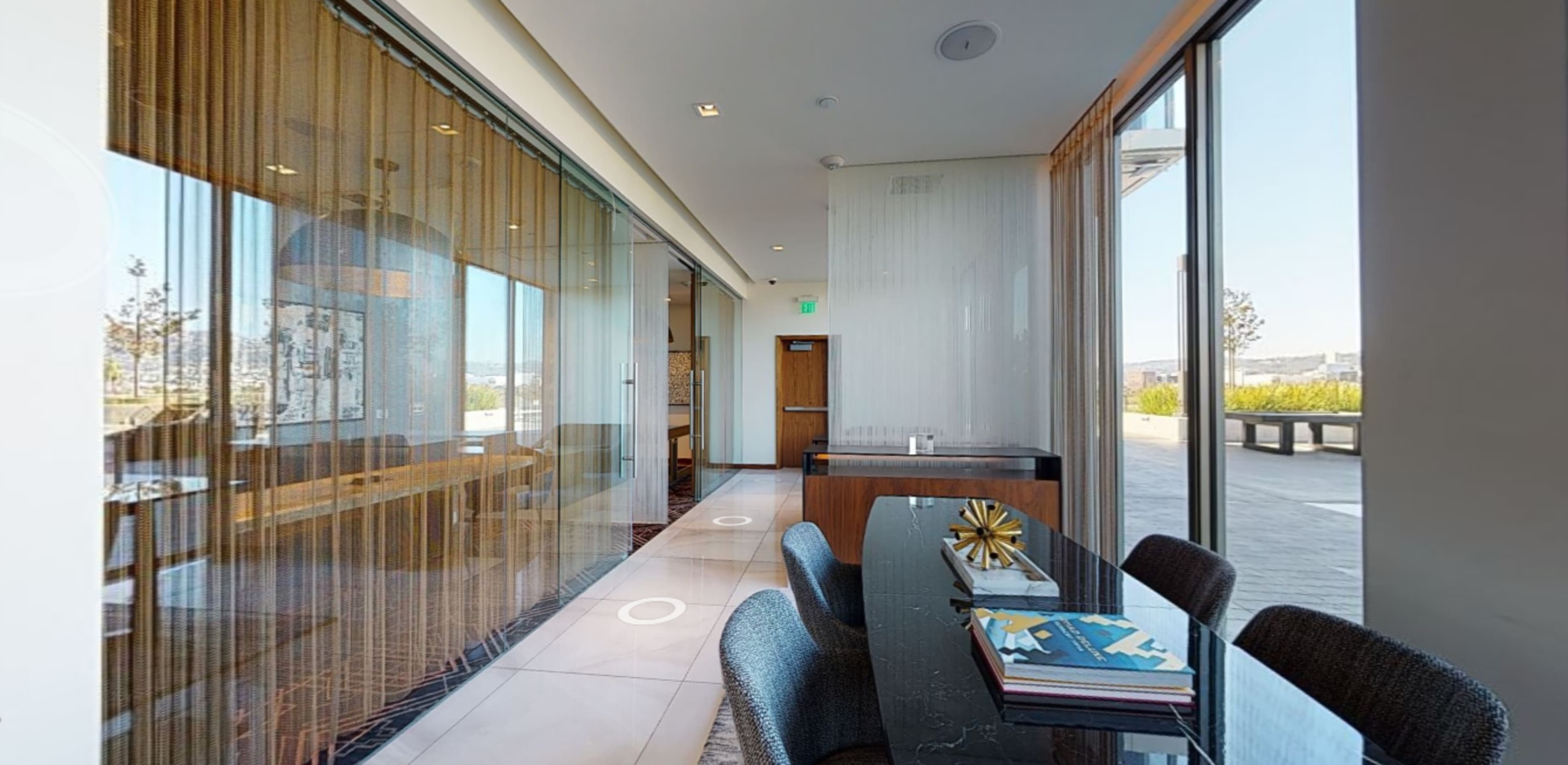 A modern interior space featuring a dining area with a large table, stylish chairs, and natural light streaming through floor-to-ceiling glass walls.