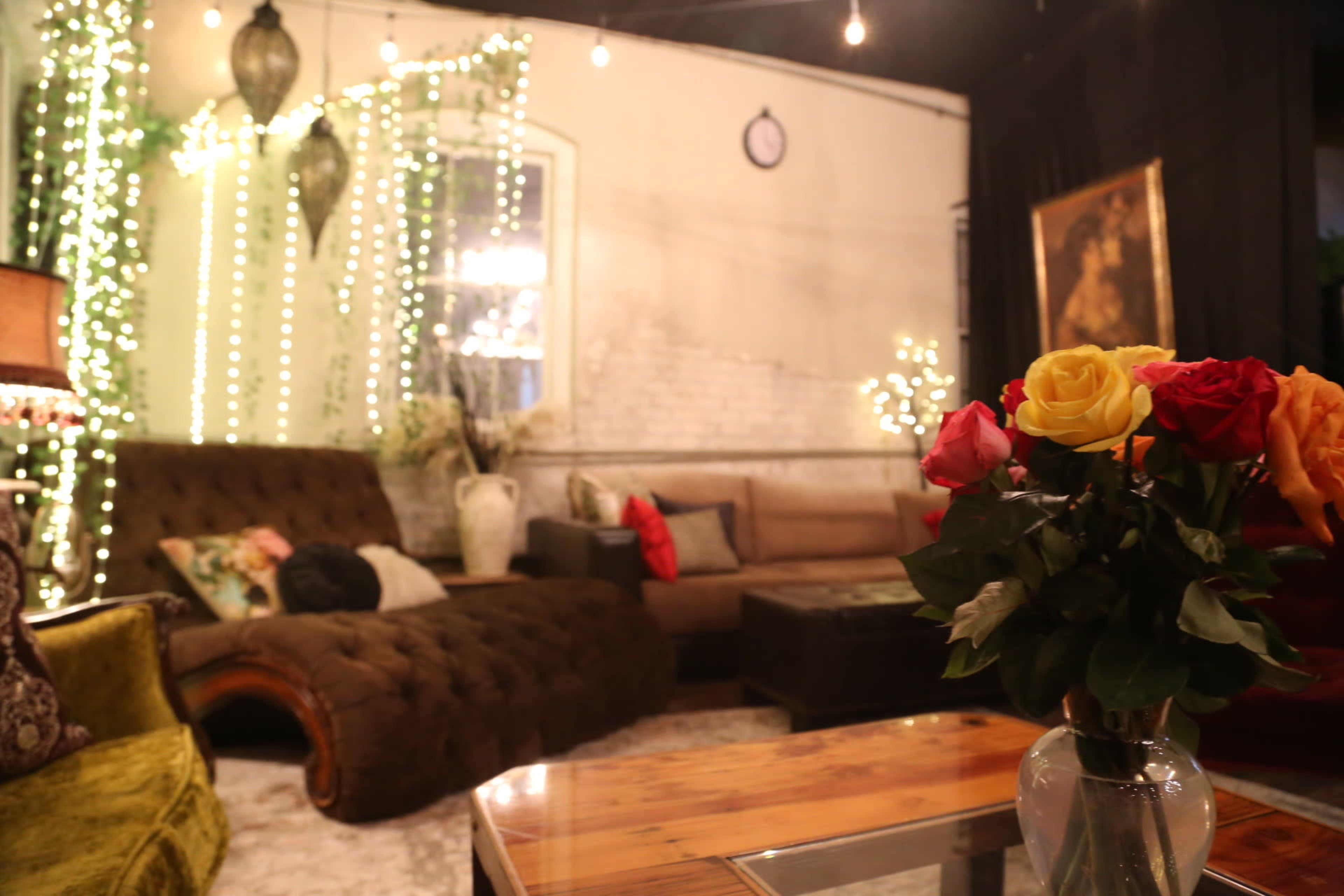 The scene features a cozy lounge area with a brown sofa, a coffee table, and decorative lights hanging from the walls, illuminated by a soft glow.