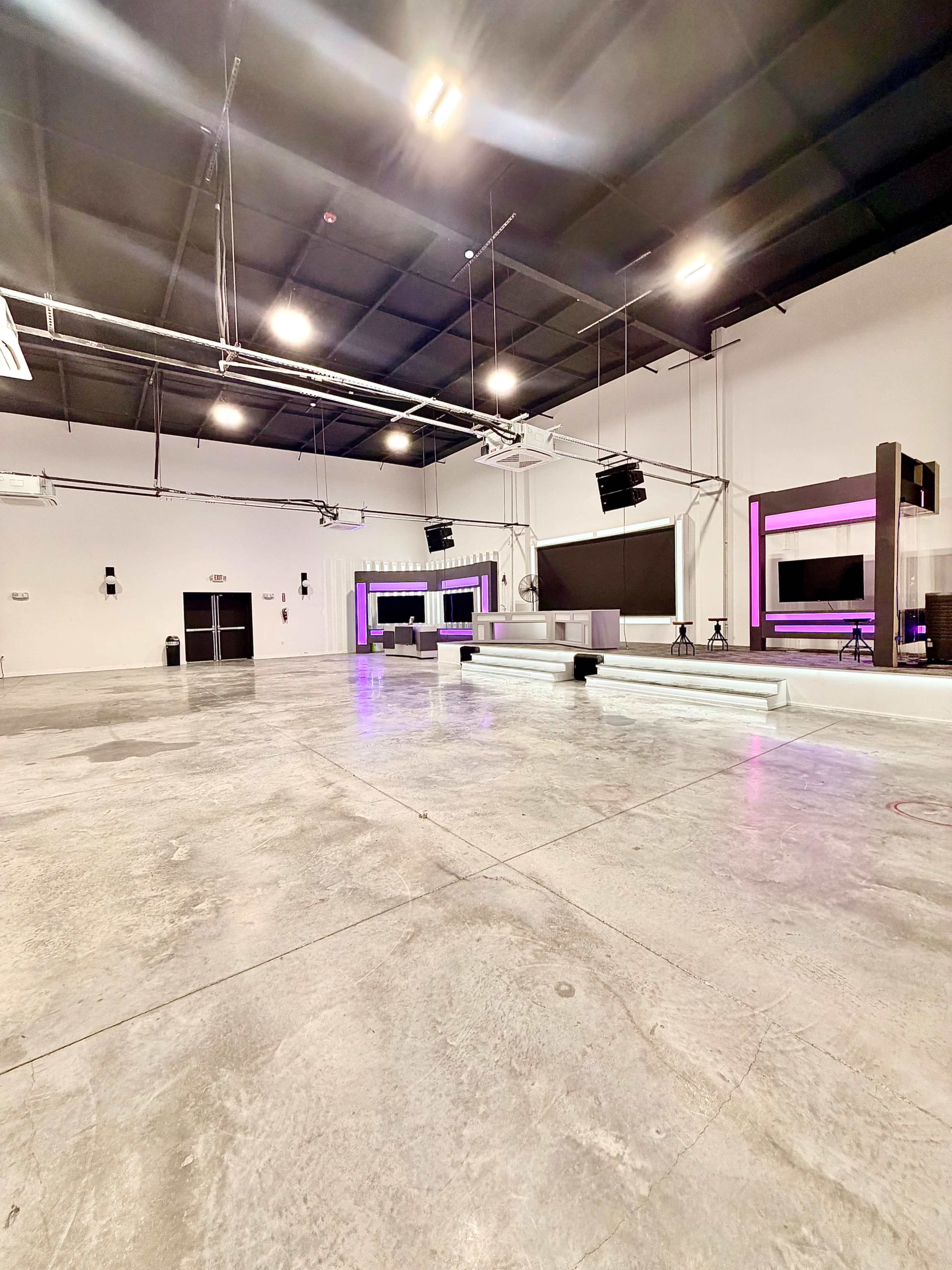 The image shows a spacious empty studio or event space with concrete flooring and modern lighting fixtures.