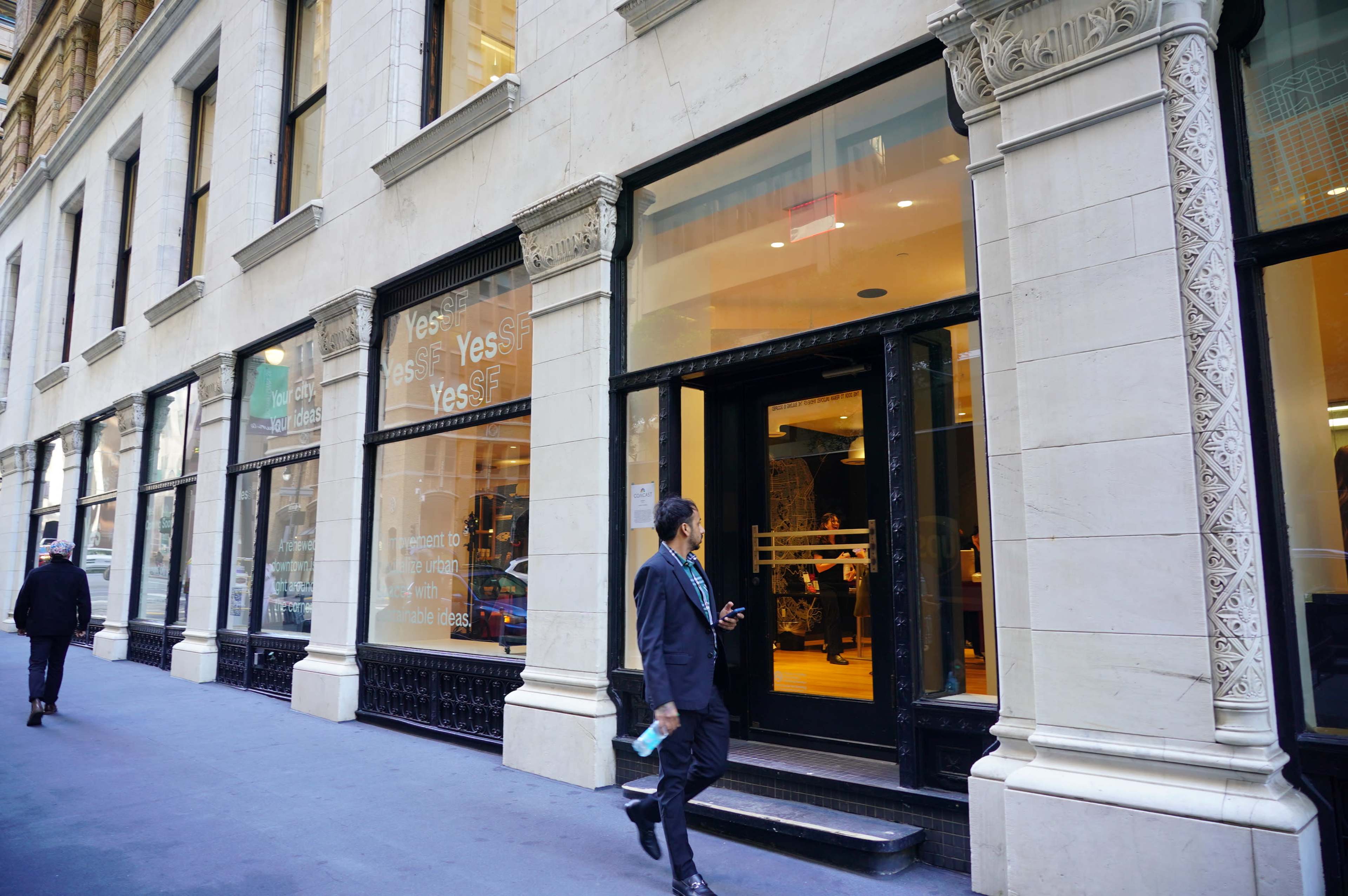 A businessman walks past a large storefront with glass windows and a sign displaying the word "Yes."