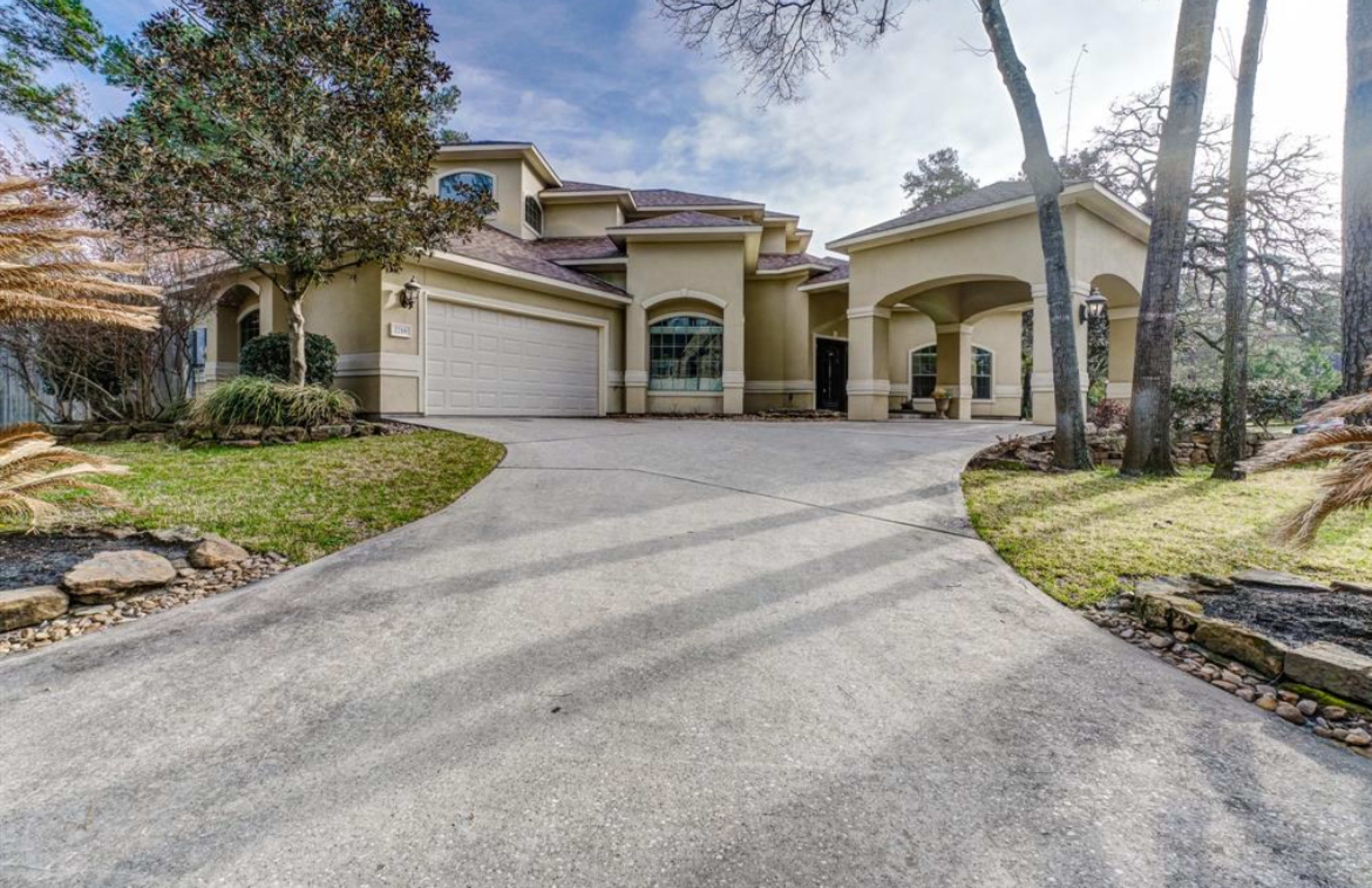 A modern house with a two-car garage and a curved driveway leading to the entrance, surrounded by greenery and landscaping.