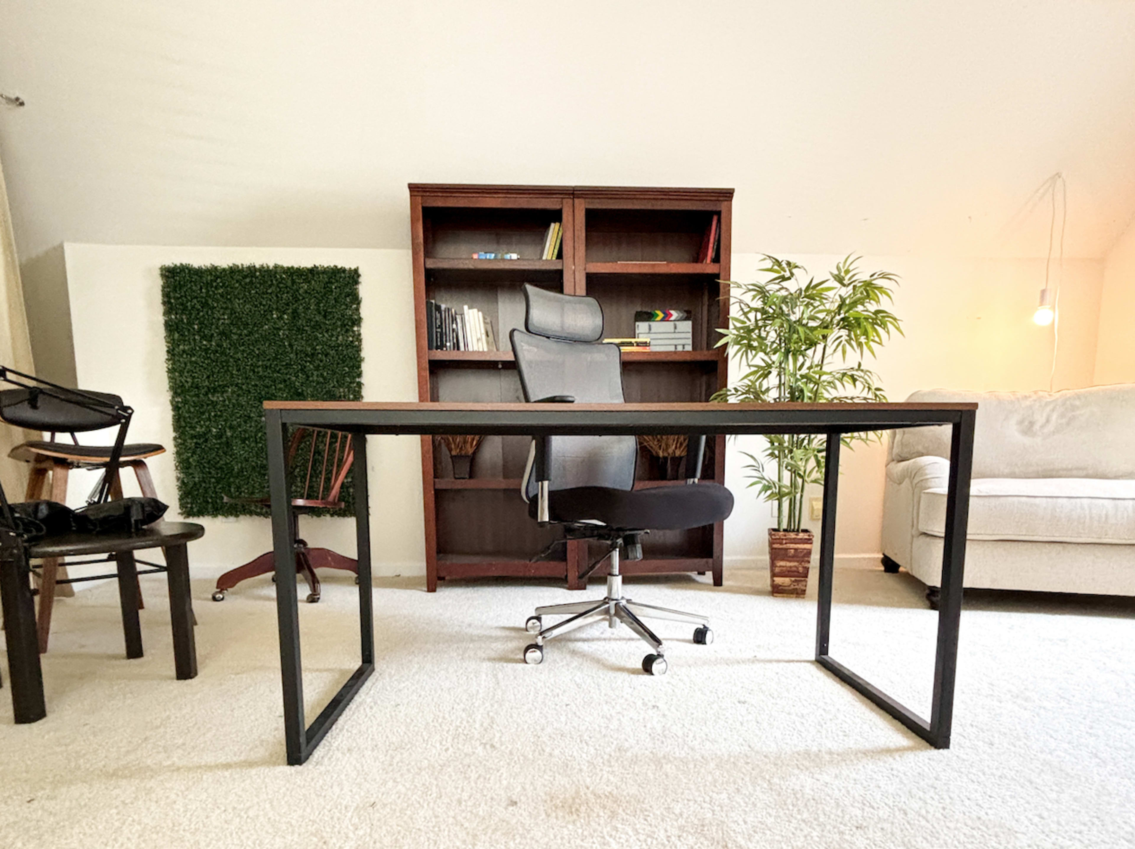 A modern office setup features a large desk with an ergonomic chair, surrounded by a bookshelf, a plant, and additional seating.