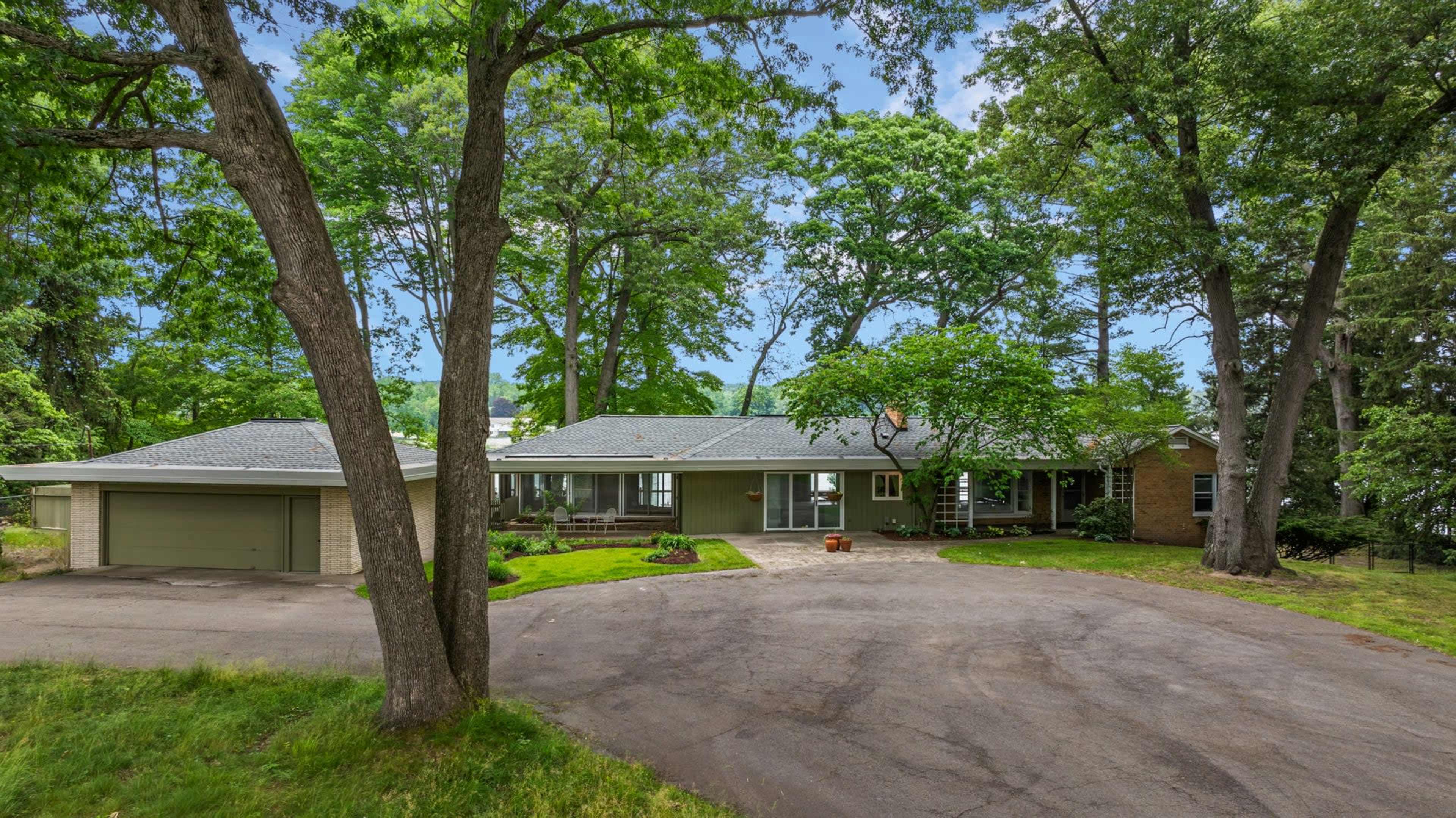 A single-story house with a landscaped front yard and a circular driveway surrounded by trees.
