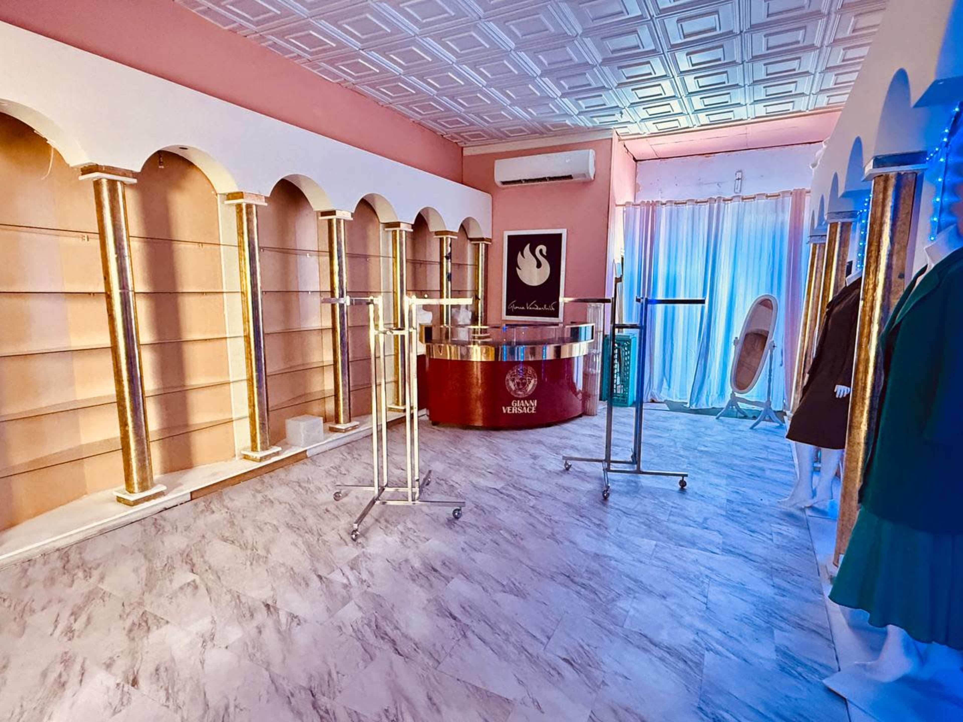 The image shows an empty boutique interior with pink walls, a reception area featuring a circular counter, and clothing racks against arched wall cutouts.