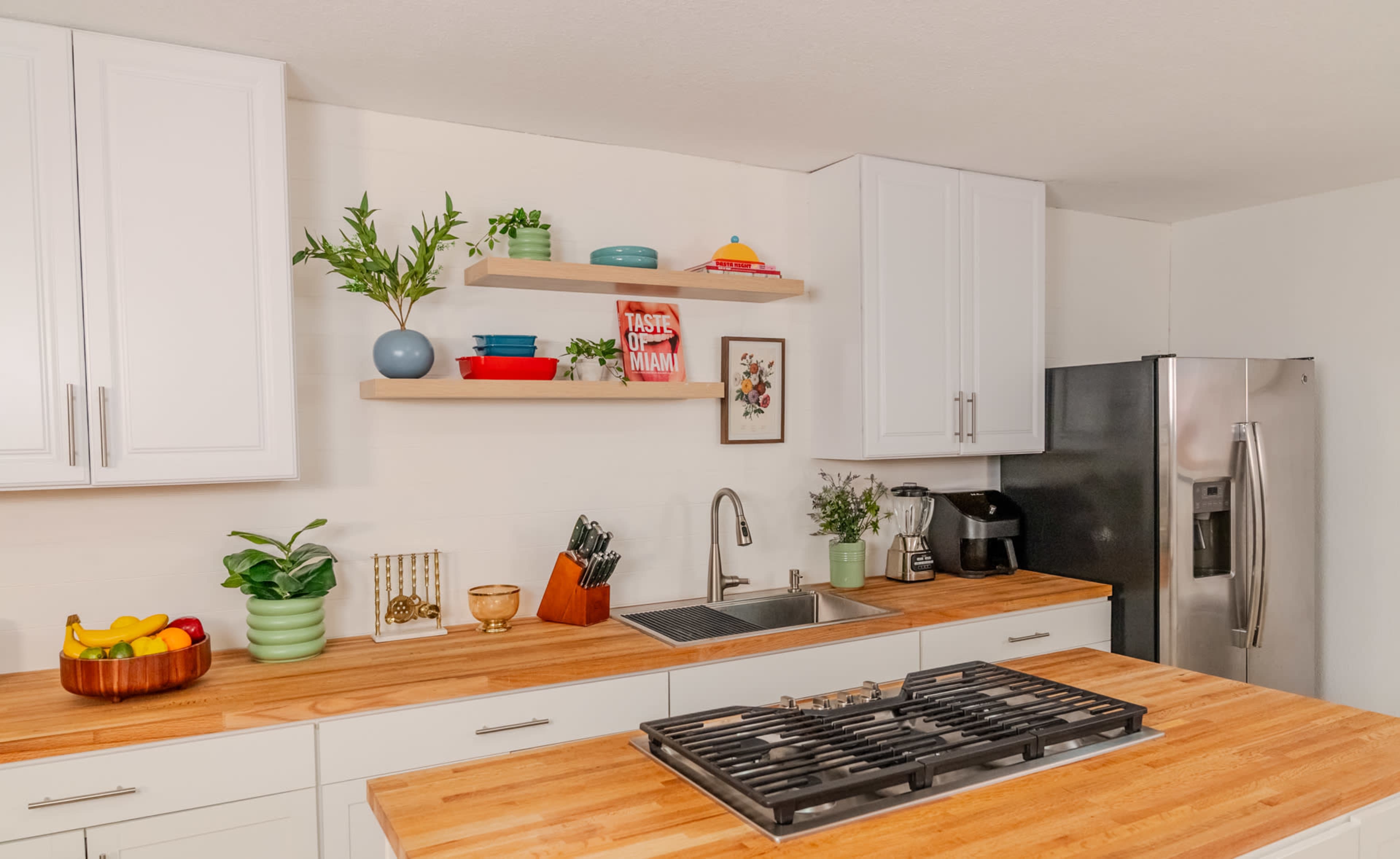 A modern kitchen features white cabinets, wooden countertops, and decorative shelving with plants and kitchenware.
