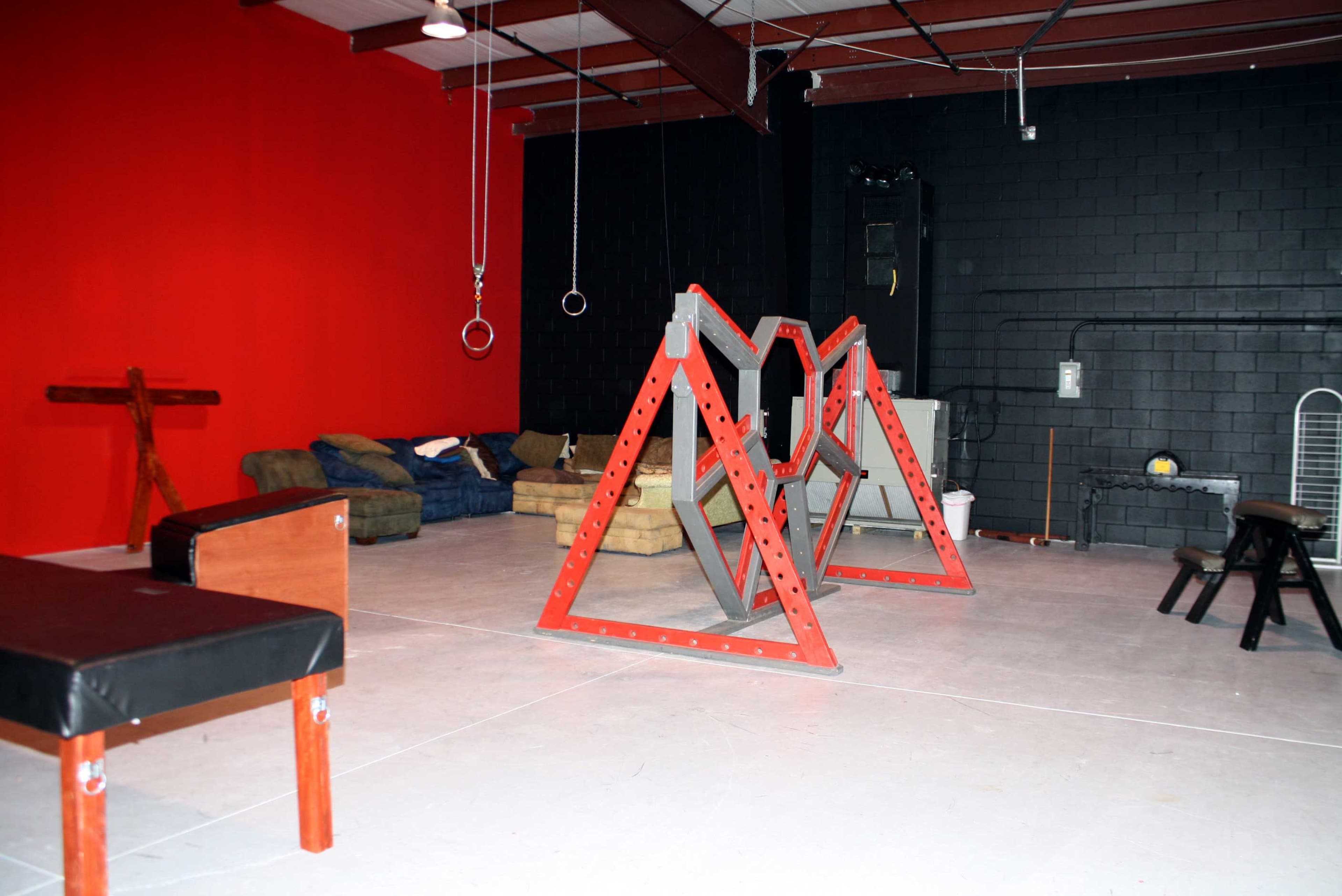 A gym space with a red and black color scheme, featuring training equipment, seating areas, and gymnastic rings suspended from the ceiling.