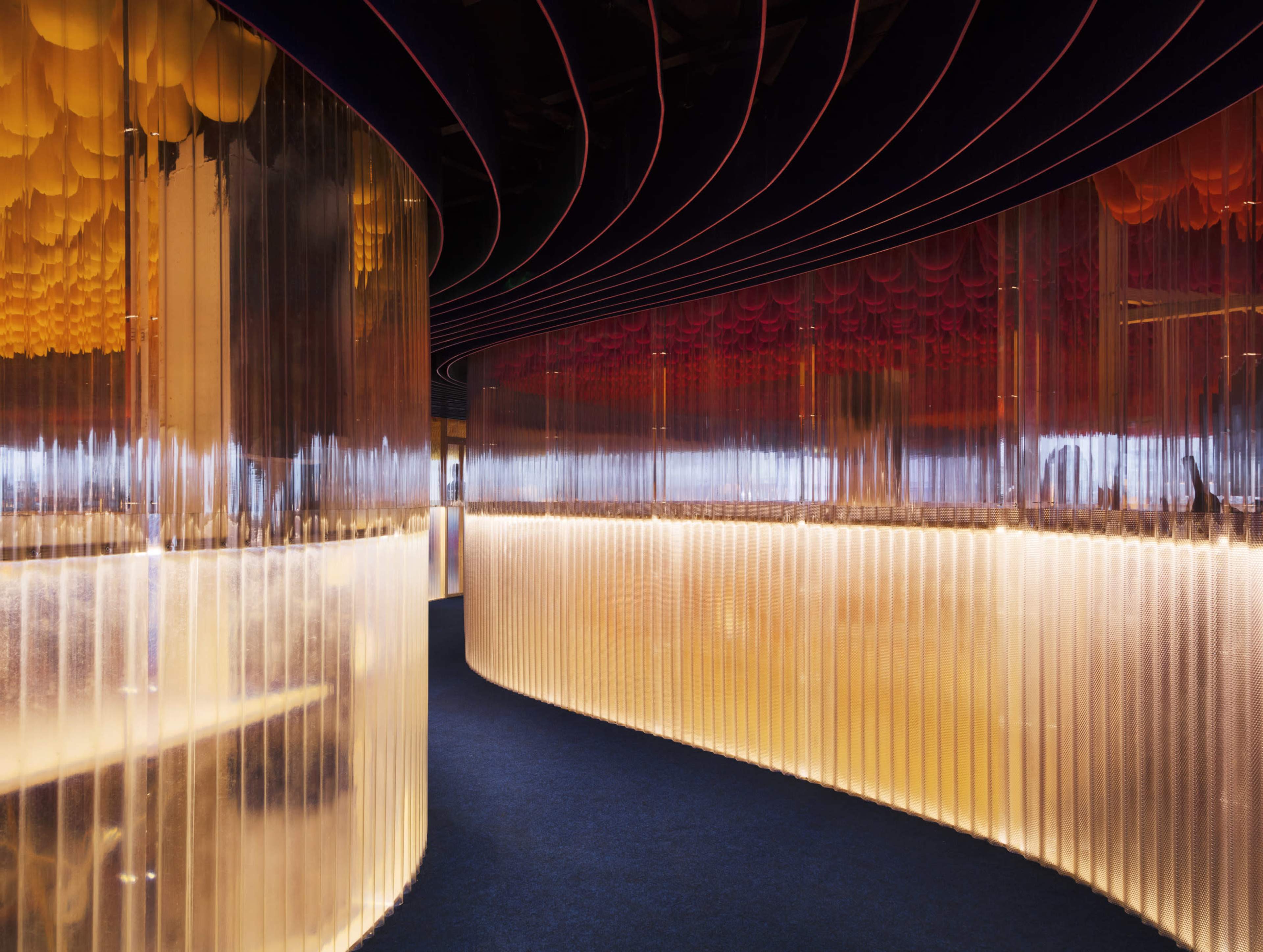 The image depicts a modern interior space featuring curved transparent walls with soft lighting and colorful ceiling panels.