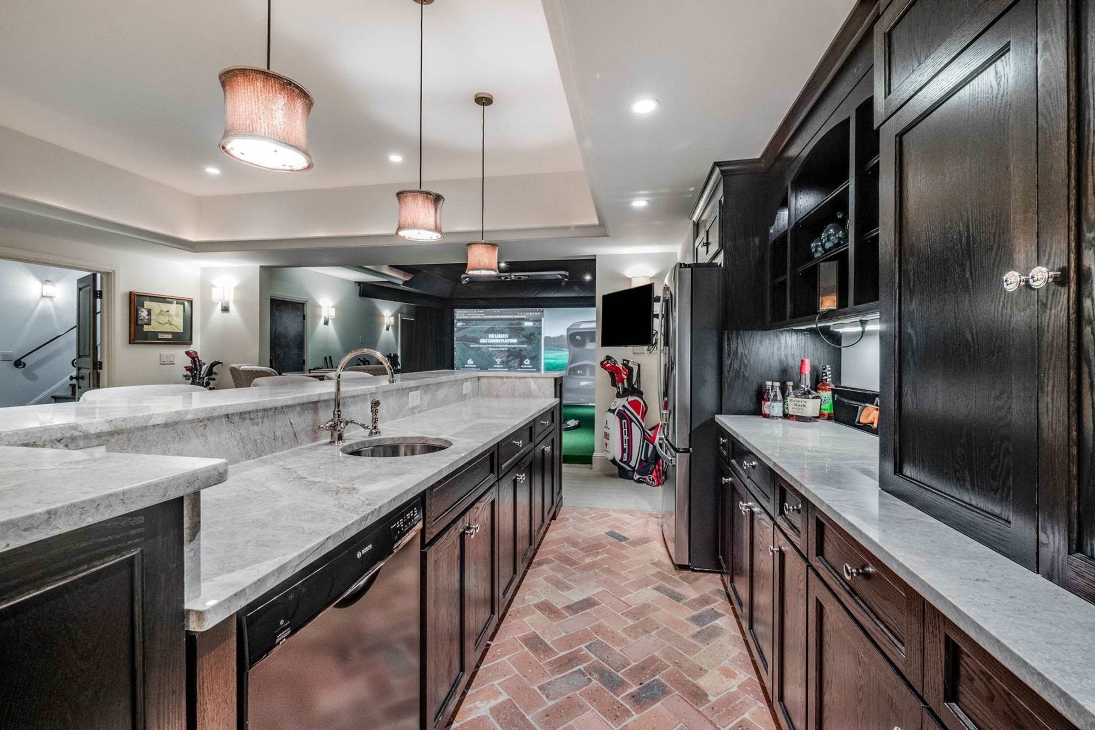 A modern kitchen with dark wooden cabinets, marble countertops, and brick flooring, featuring a sink and kitchen appliances in the background.