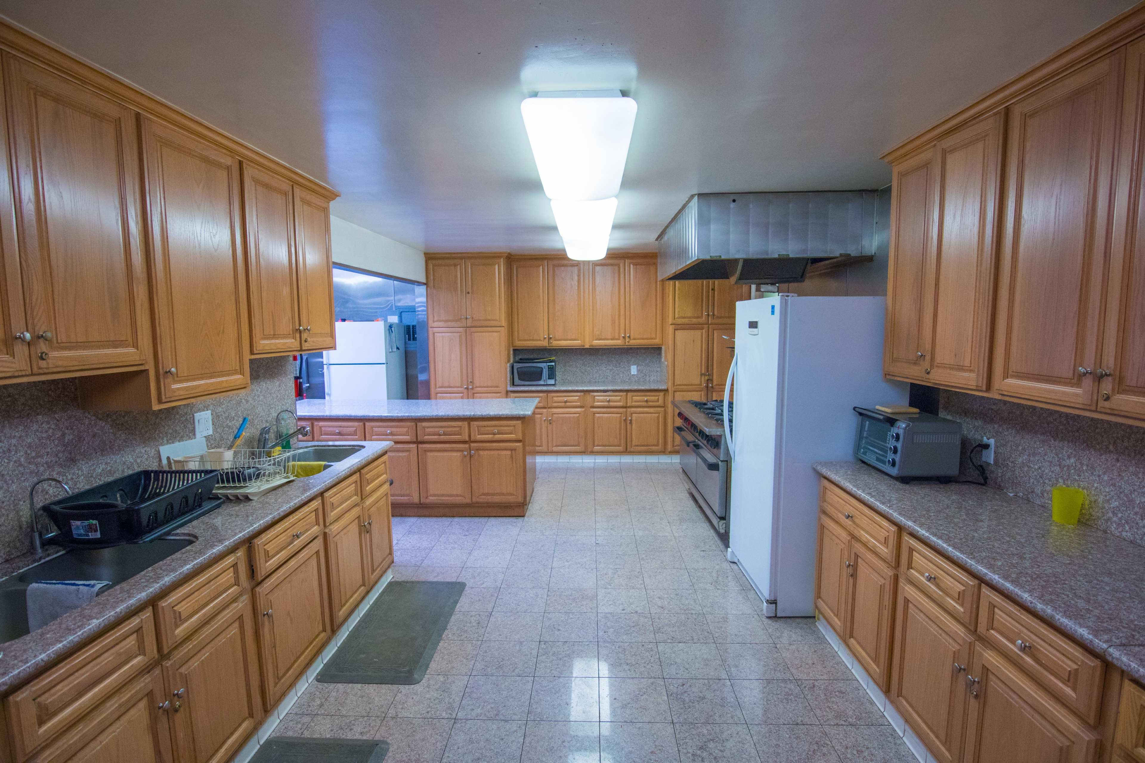A spacious kitchen with wooden cabinets, a white refrigerator, and equipment for cooking and dishwashing.