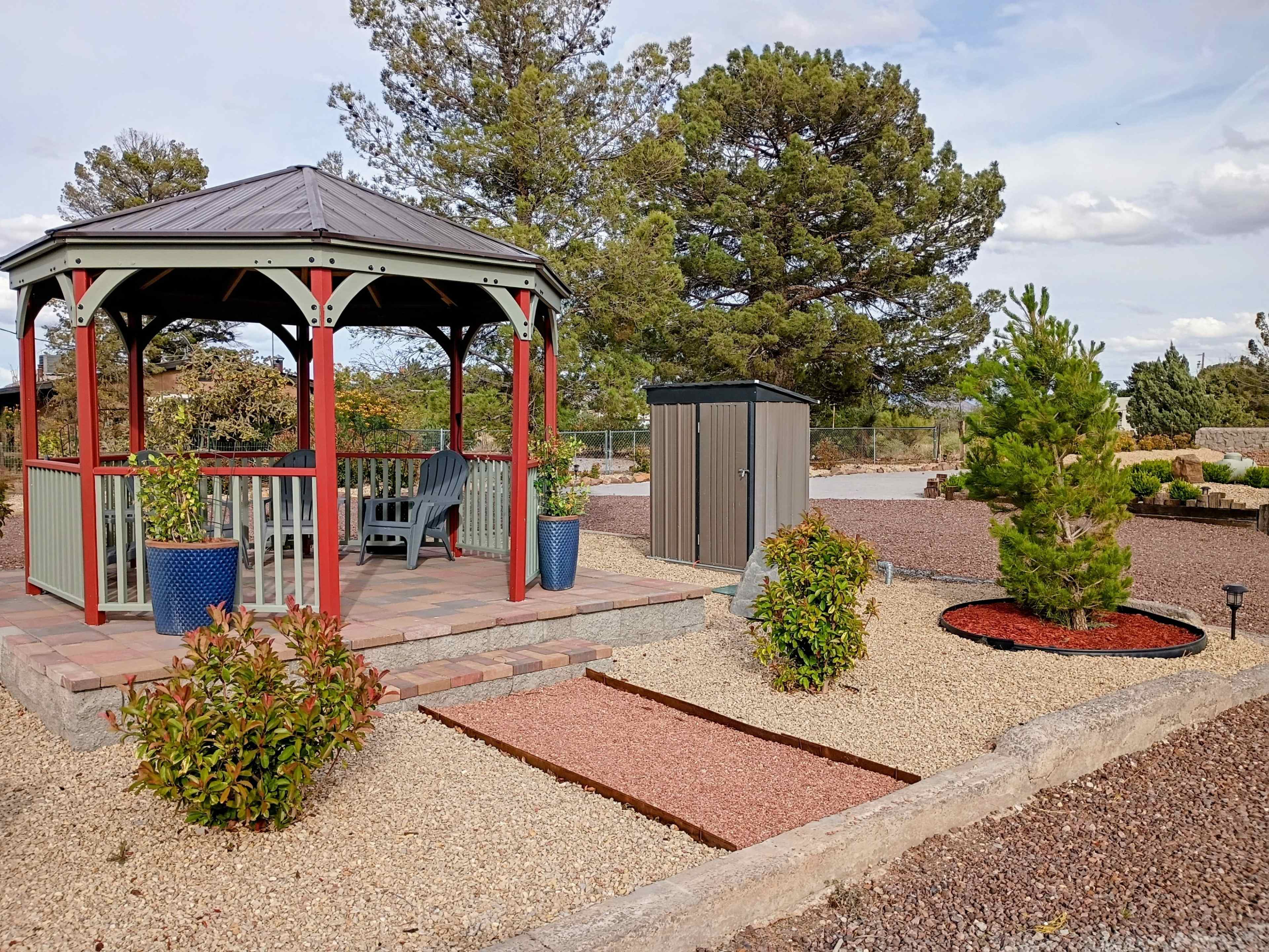 The image features a gazebo surrounded by gravel landscaping, a small storage shed, and decorative plants.