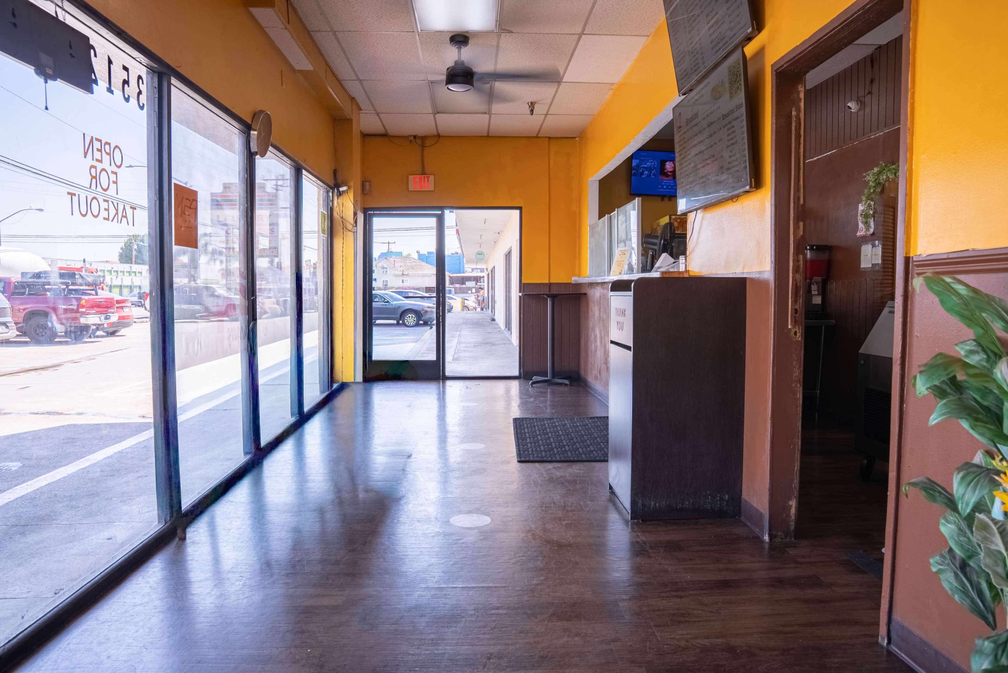 The image shows the interior of a restaurant with a counter and a view through the entrance leading to an outdoor area.