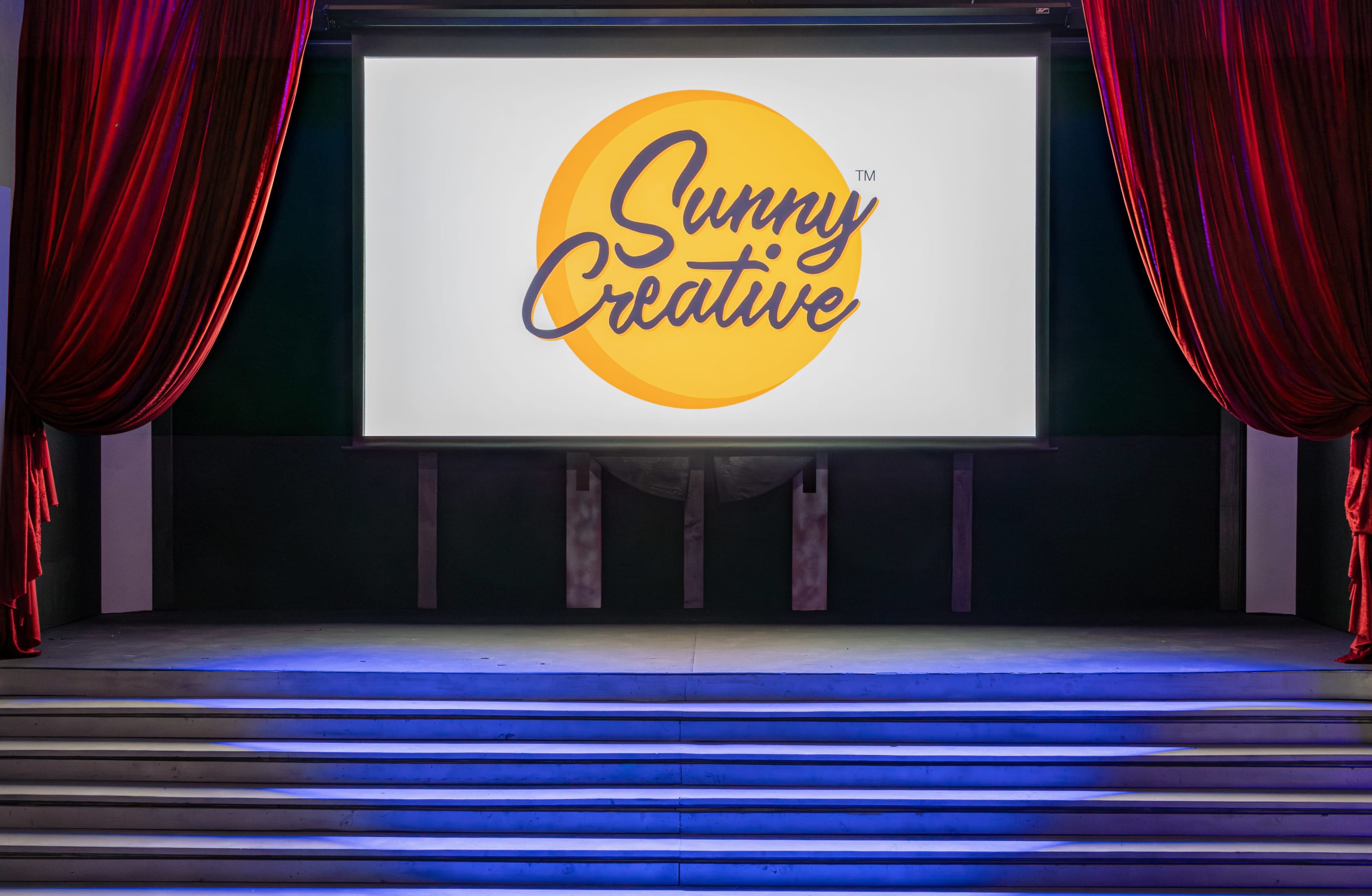 A stage with red curtains, featuring a large screen displaying the logo for "Sunny Creative."