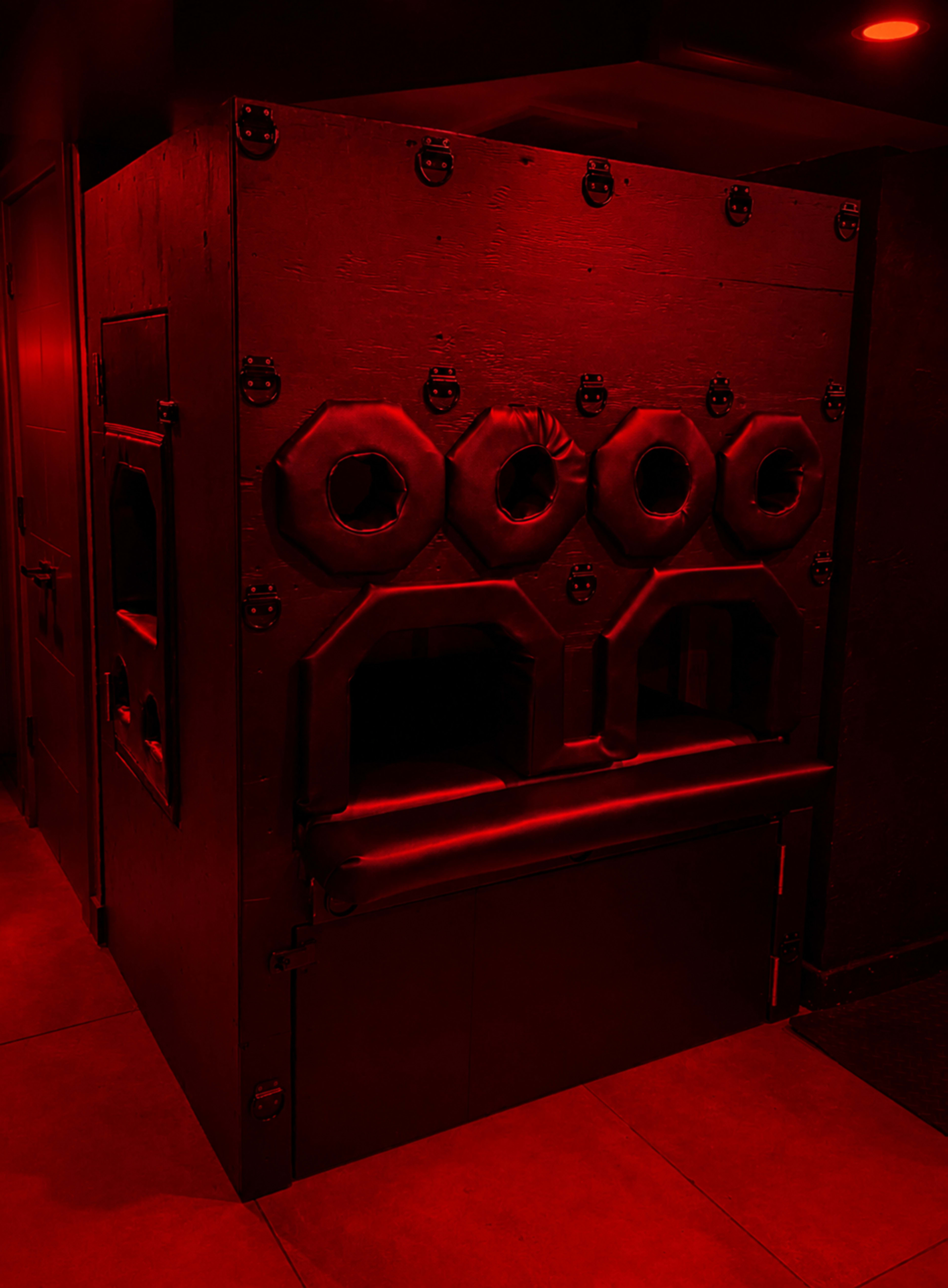The image shows a dark room featuring a red-lit apparatus with multiple circular openings, resembling a structured enclosure.