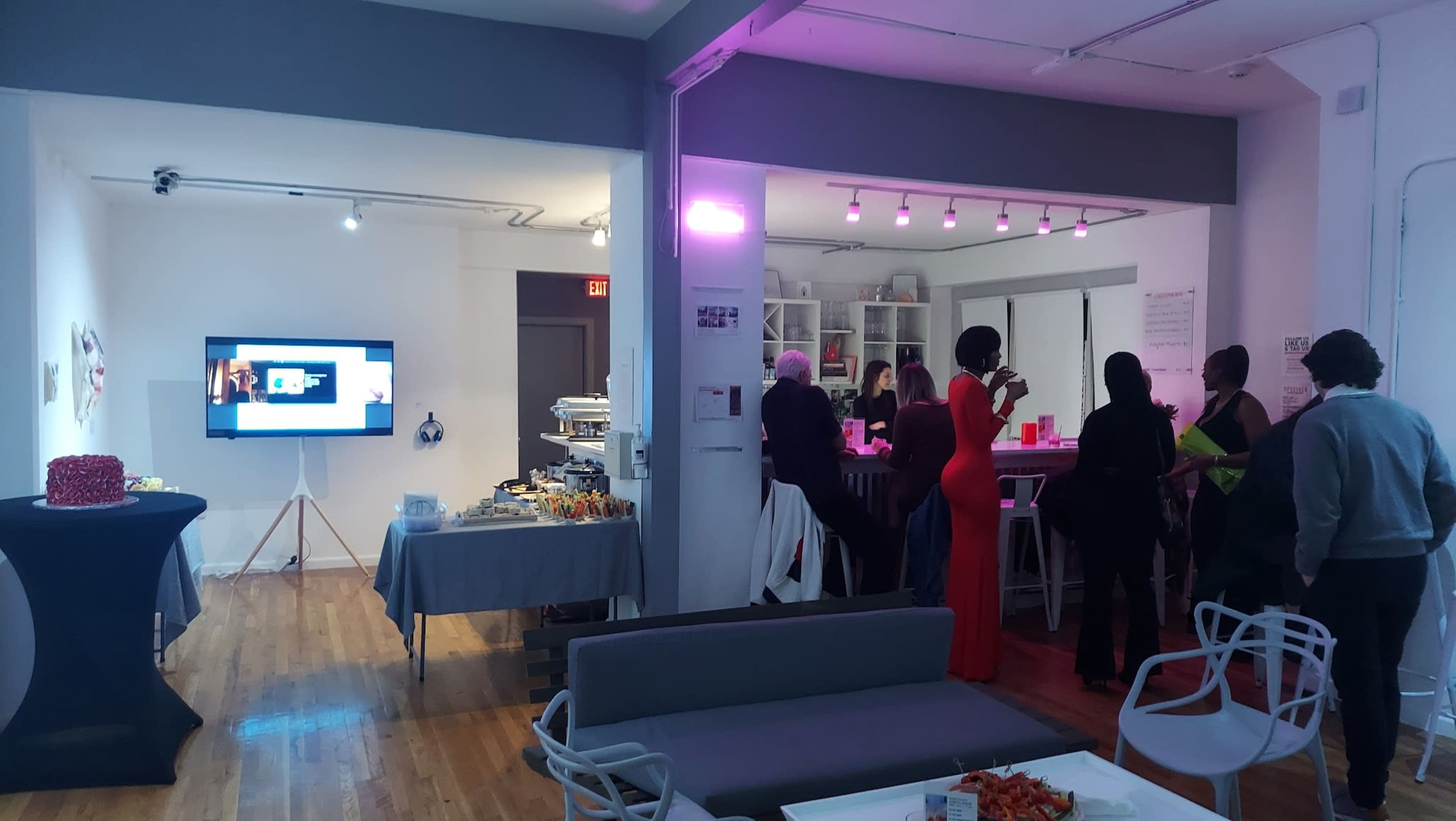 A gathering in a spacious room with a buffet on one side, a bar area in the center, and guests mingling around.