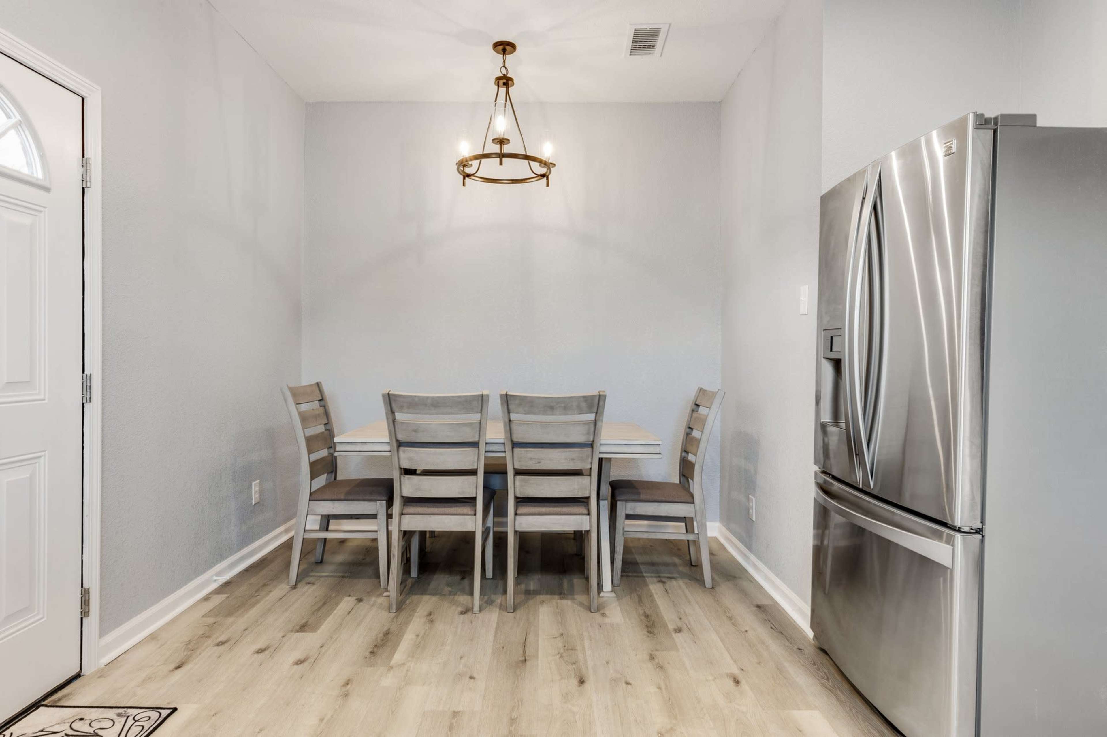 A dining area features a wooden table and six chairs next to a stainless steel refrigerator.