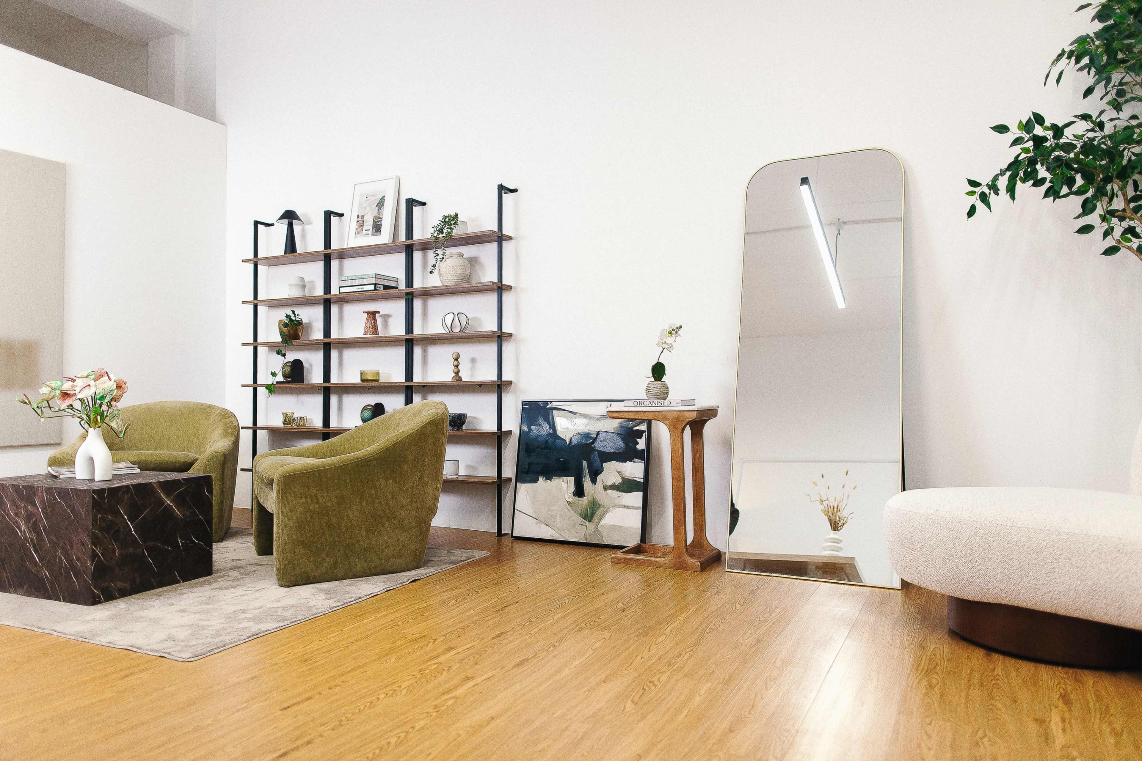 The image shows a modern interior space featuring two green armchairs, a coffee table, a bookshelf, a large mirror, and decorative elements on the walls and floor.