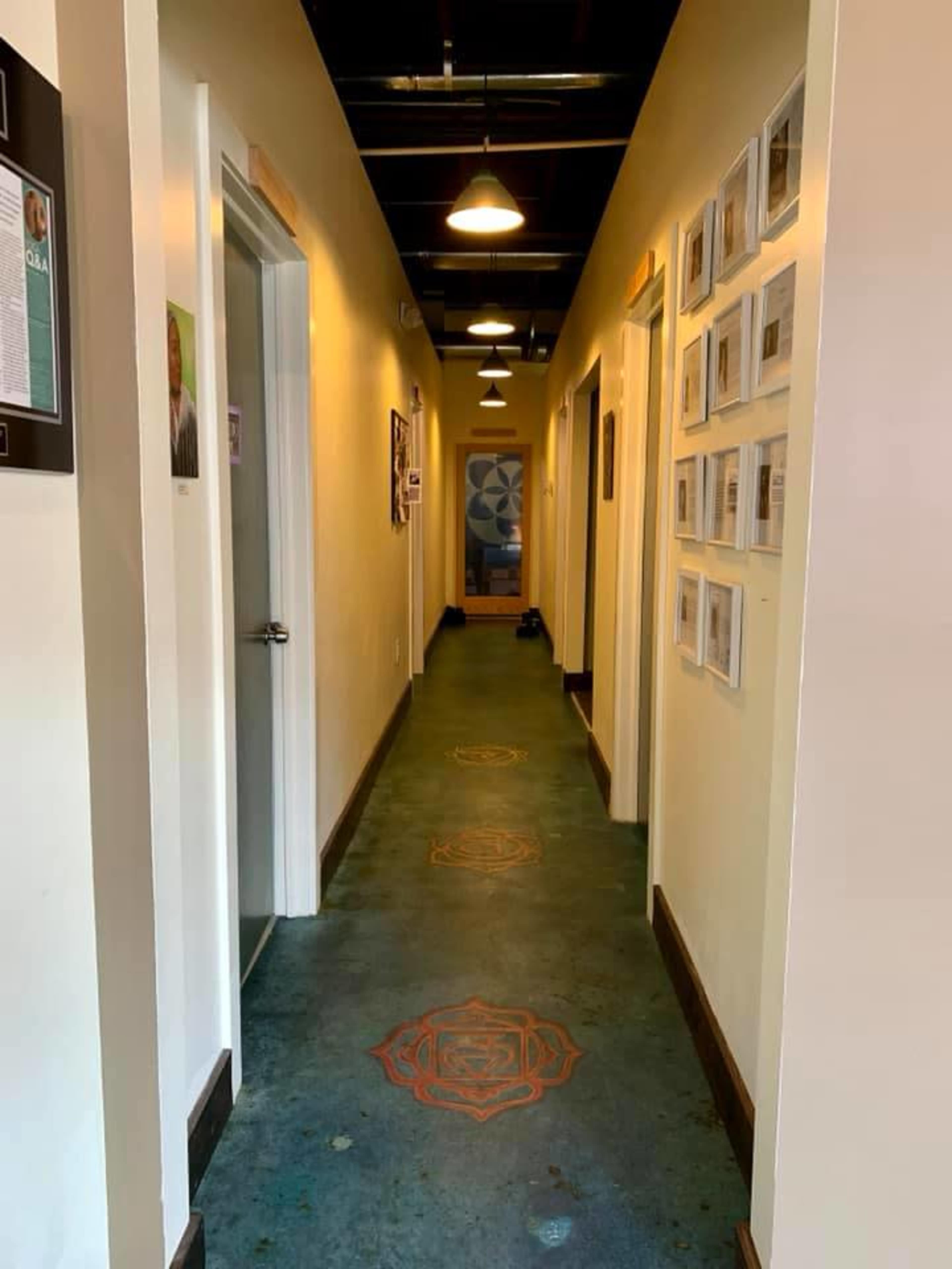 A narrow hallway lined with doors on either side and framed photographs on the wall.
