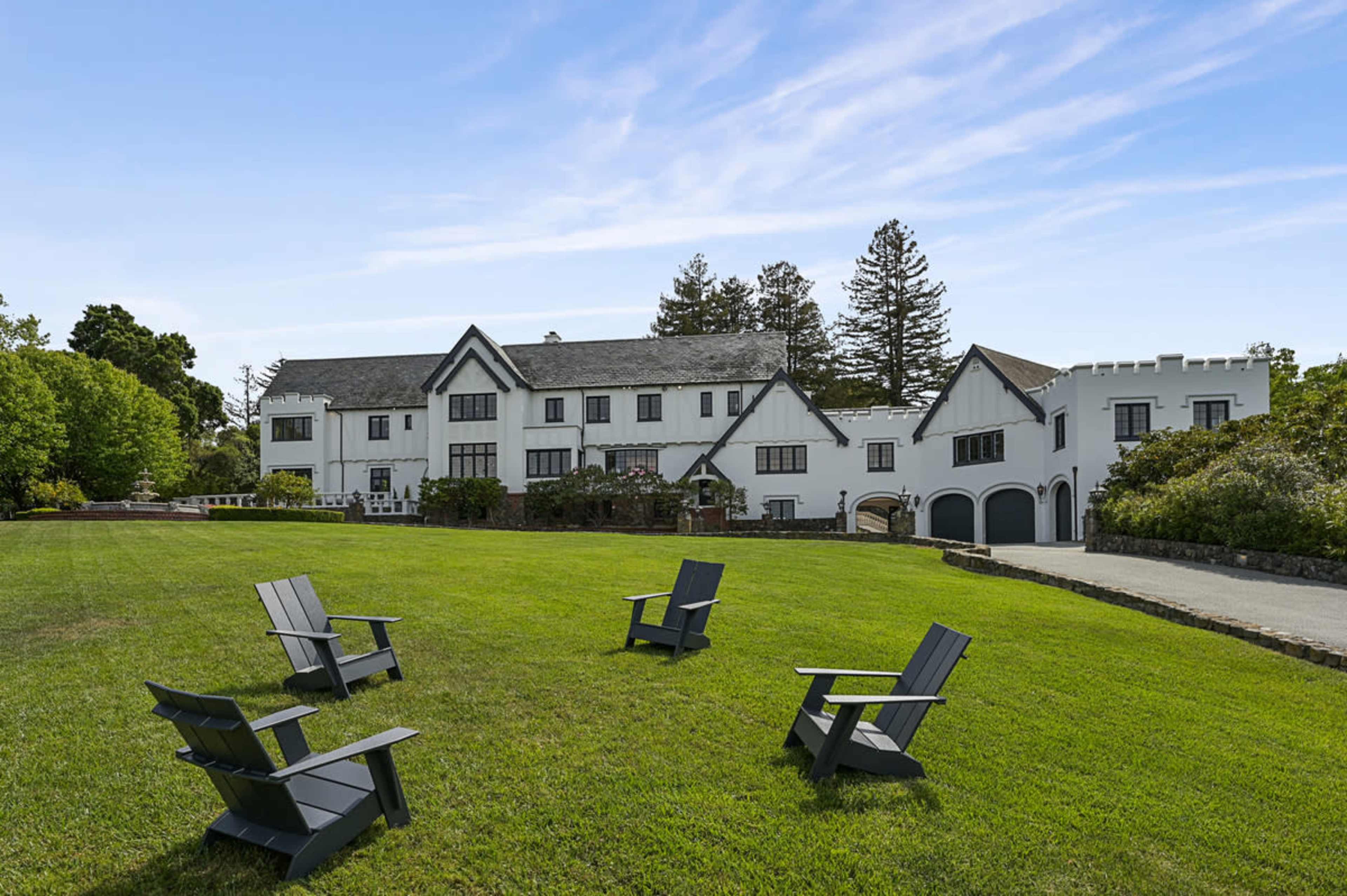 A large white mansion with a landscaped lawn features several black wooden chairs arranged on the grass.