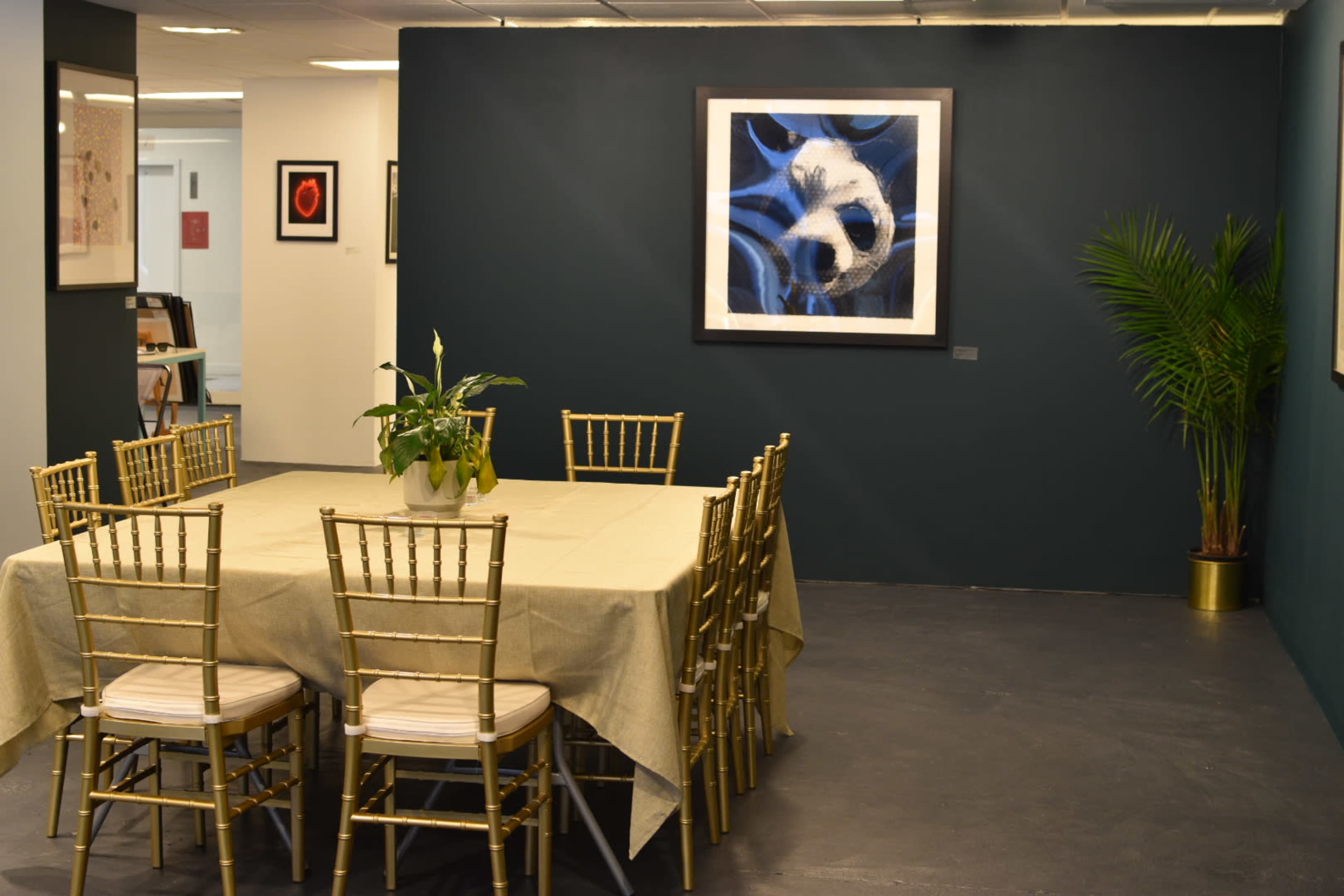 The image shows a conference room with a gold-accented table surrounded by chairs and a framed artwork on a dark blue wall.