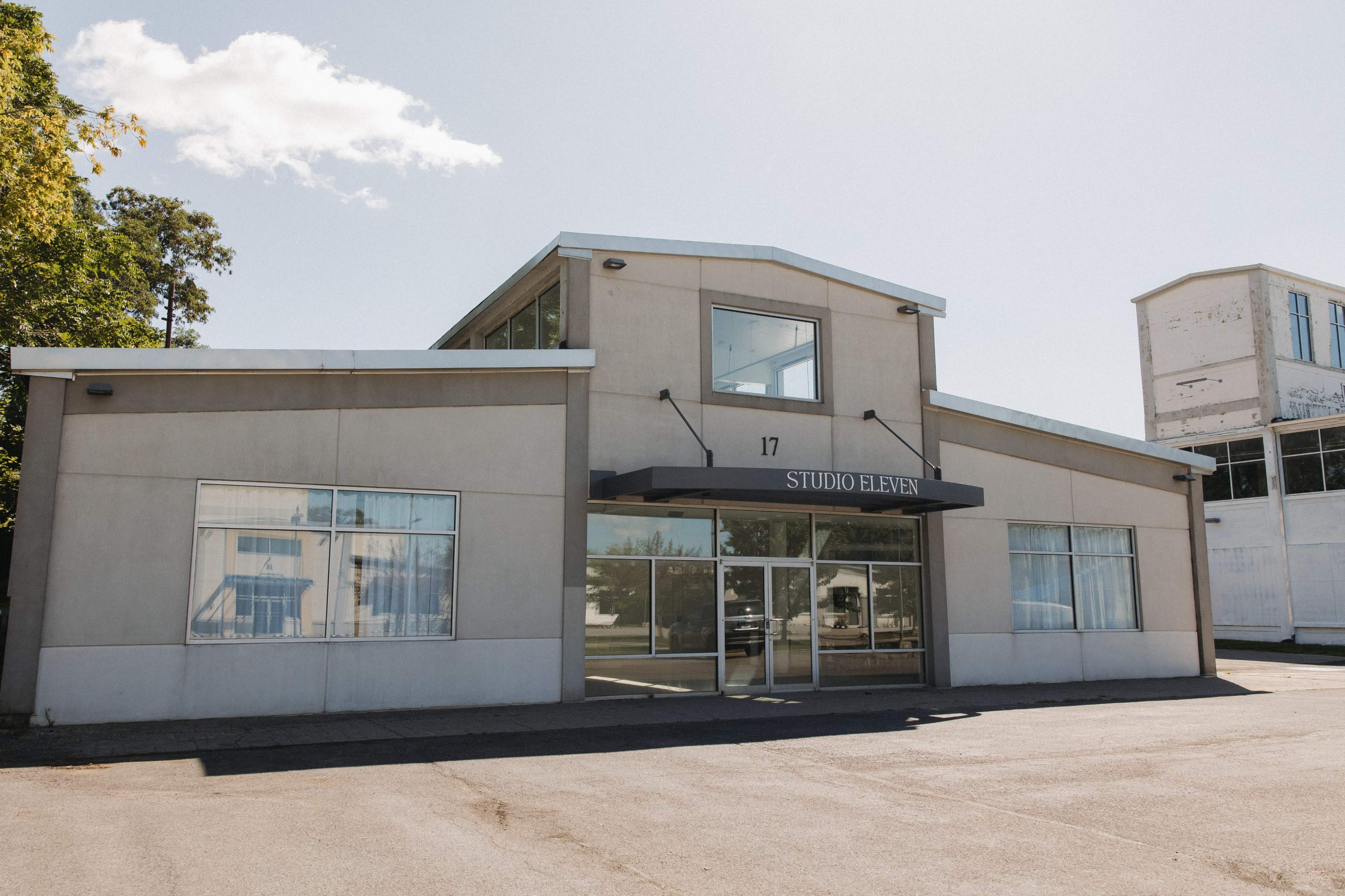 The image shows a modern two-story building with large windows and a sign that reads "STUDIO ELEVEN" above the entrance.