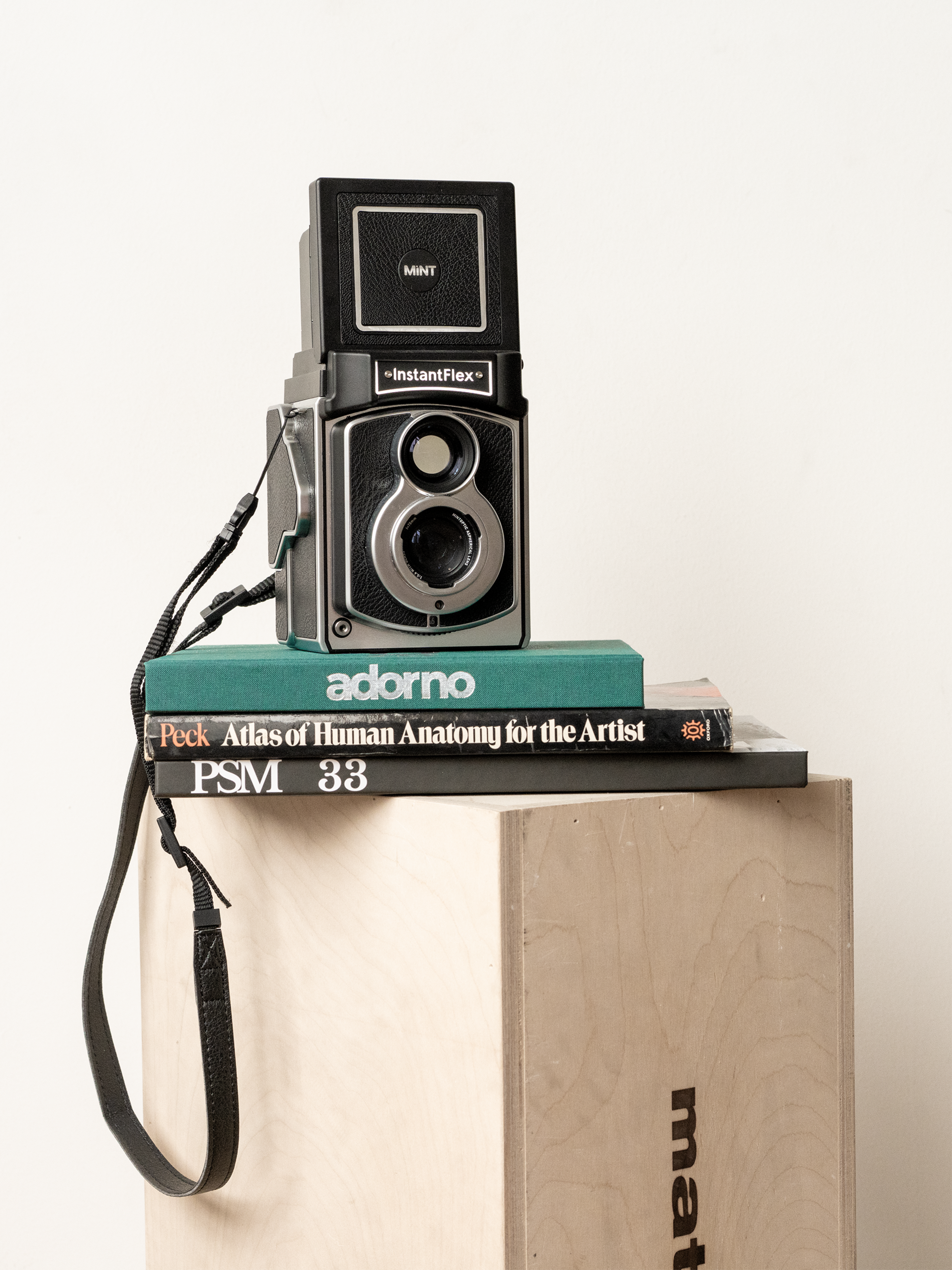 A vintage instant camera is placed on top of a stack of books on a wooden crate.