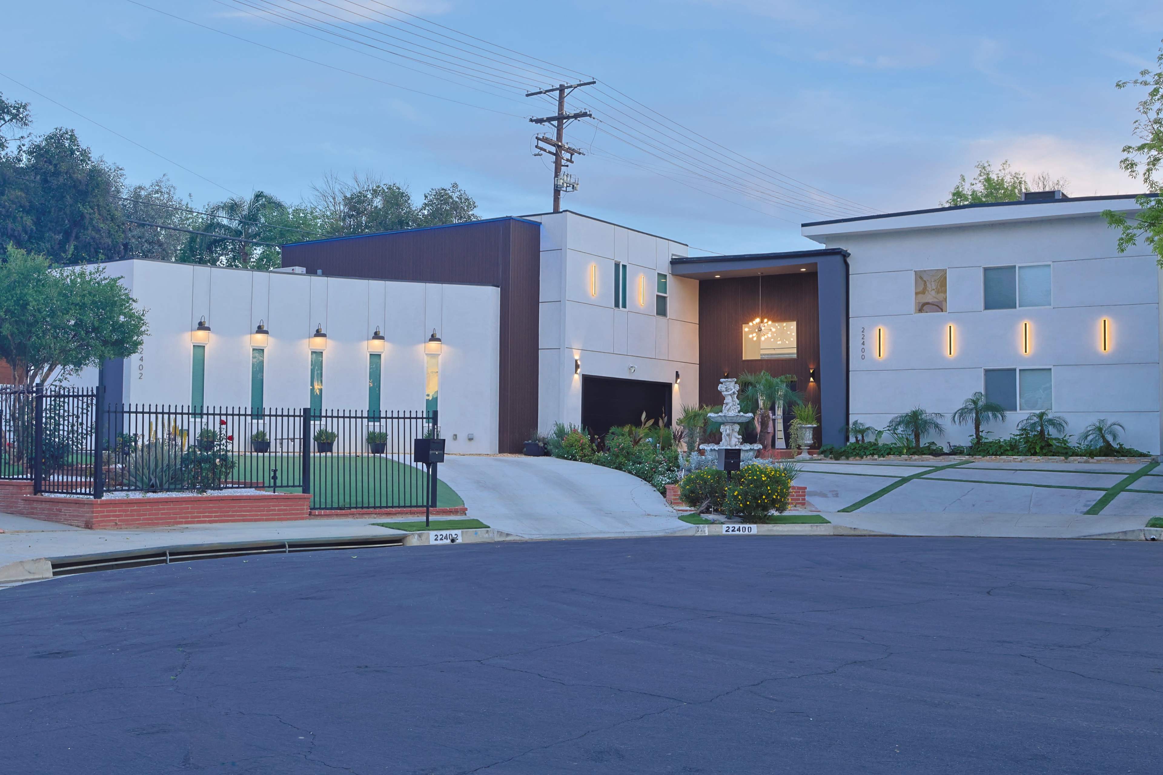 The image shows a modern two-story house with a gated entrance, featuring a mix of materials and large windows, situated at the end of a cul-de-sac.