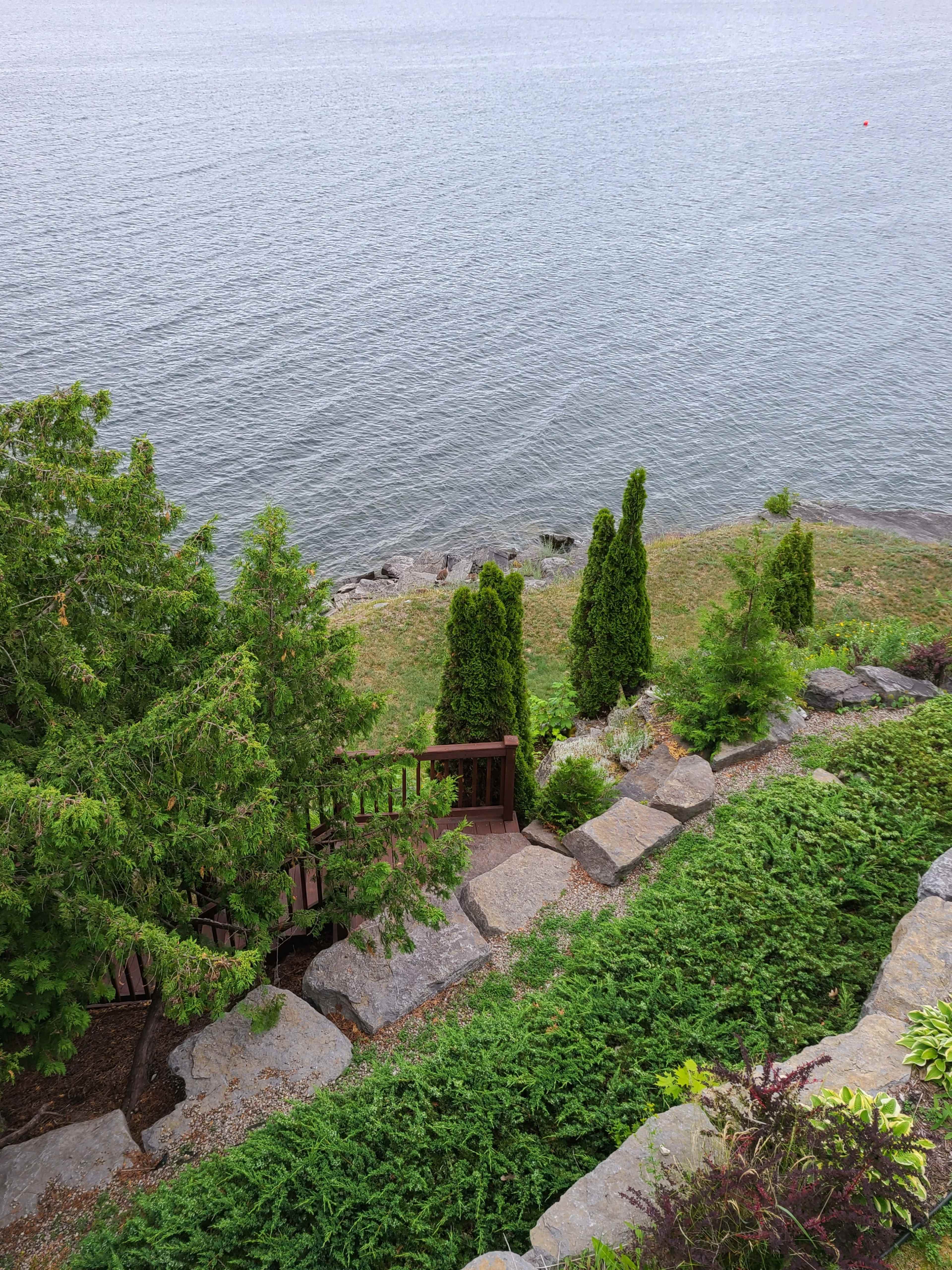 A stone pathway leads down through greenery to a rocky shore along a calm body of water.