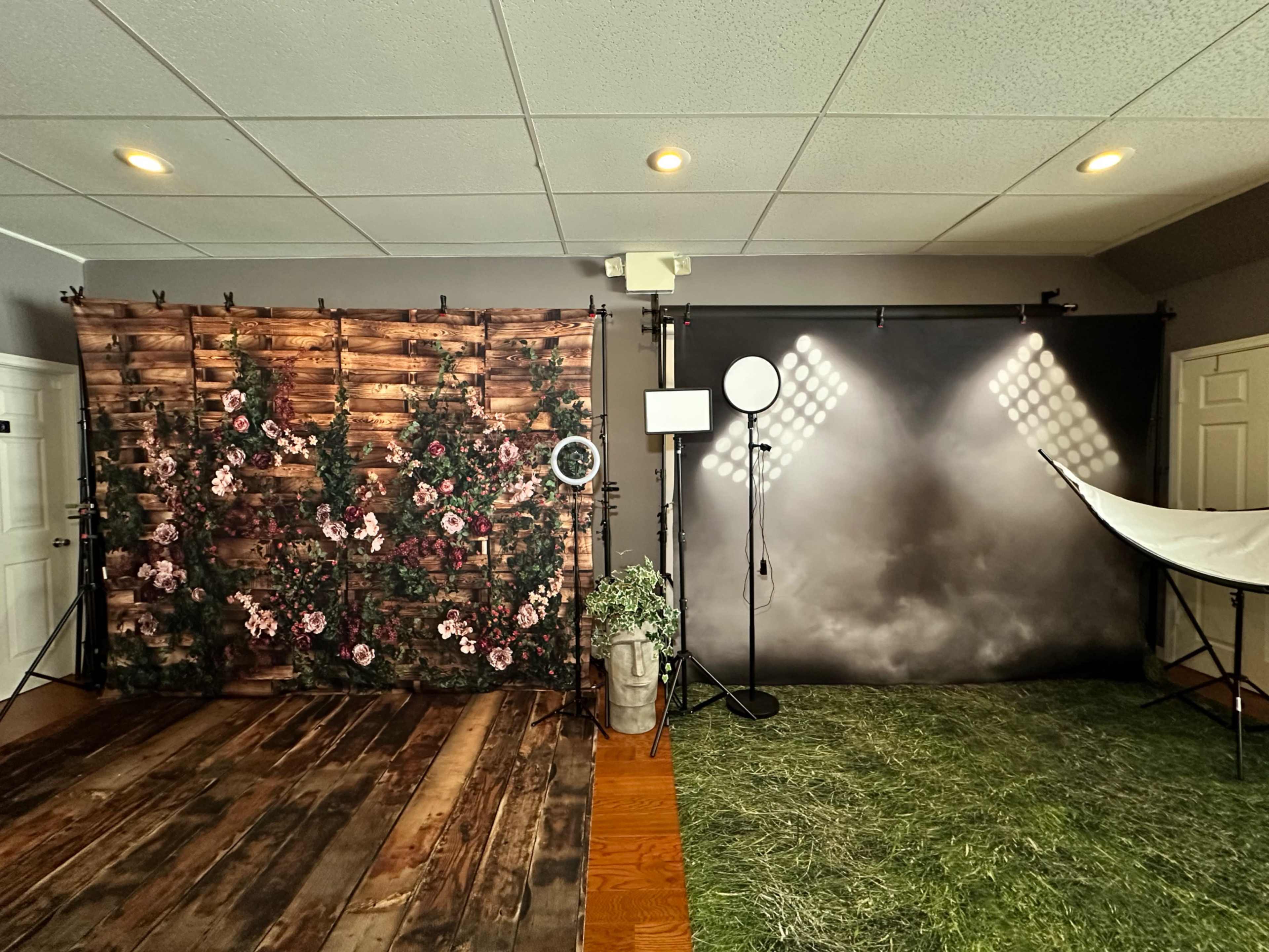 A photography studio with two distinct backgrounds: one featuring floral decorations on a wooden backdrop and the other a plain gray backdrop with bright lighting.