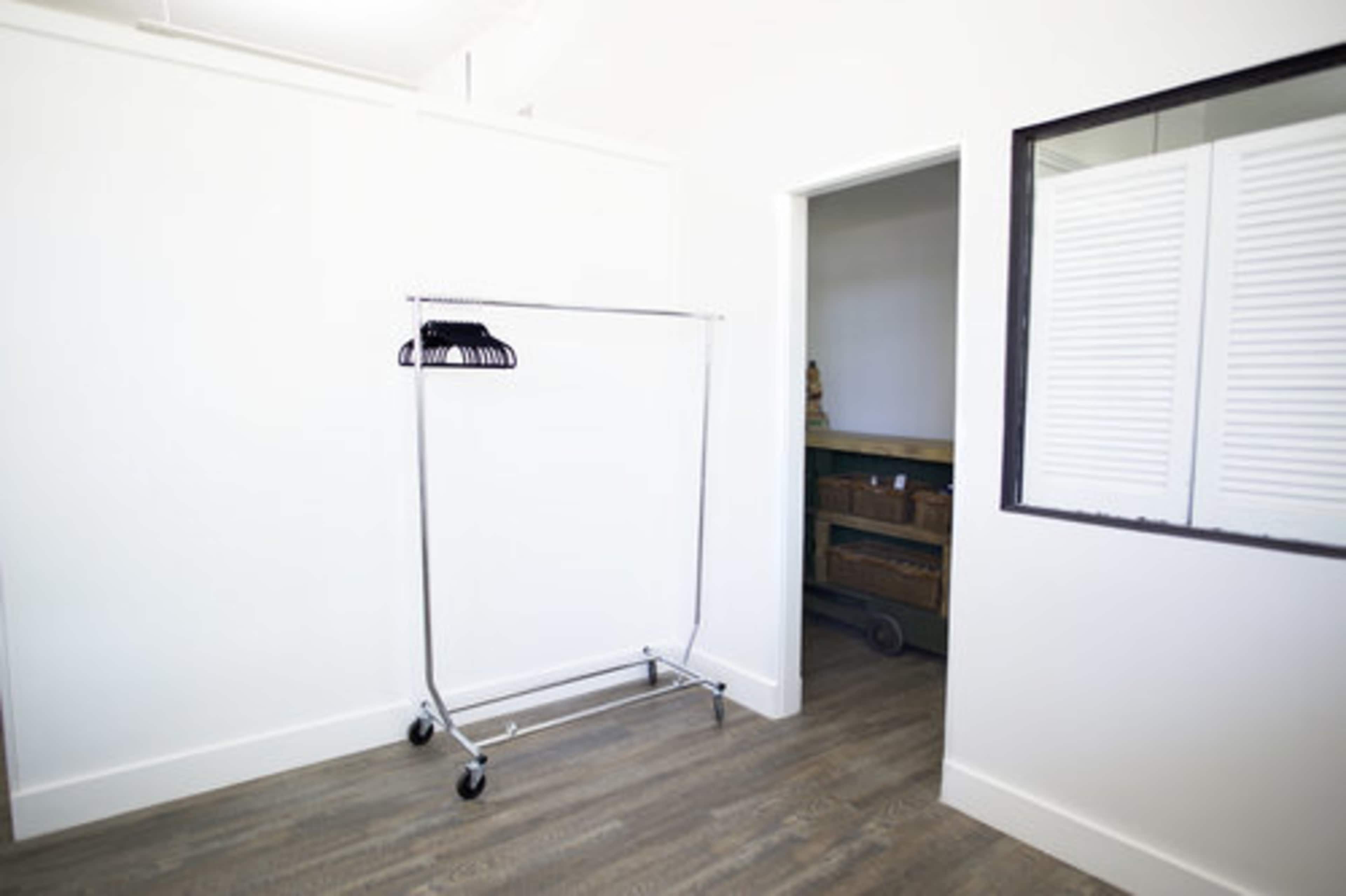 An empty clothing rack stands in a minimalist room with a doorway leading to another space.
