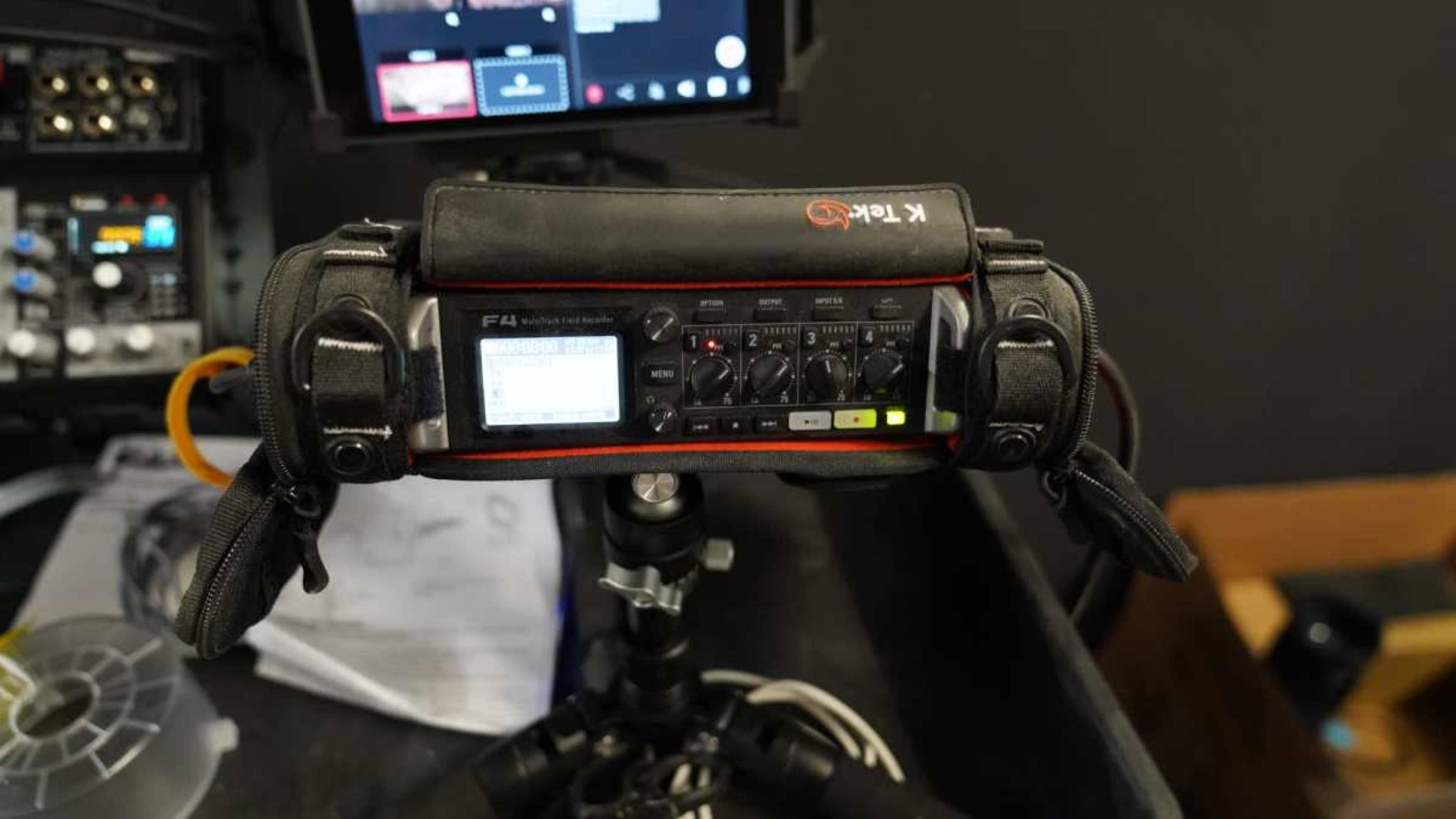 The image displays a Zoom F4 audio recorder mounted on a tripod, surrounded by various audio equipment in a studio setting.