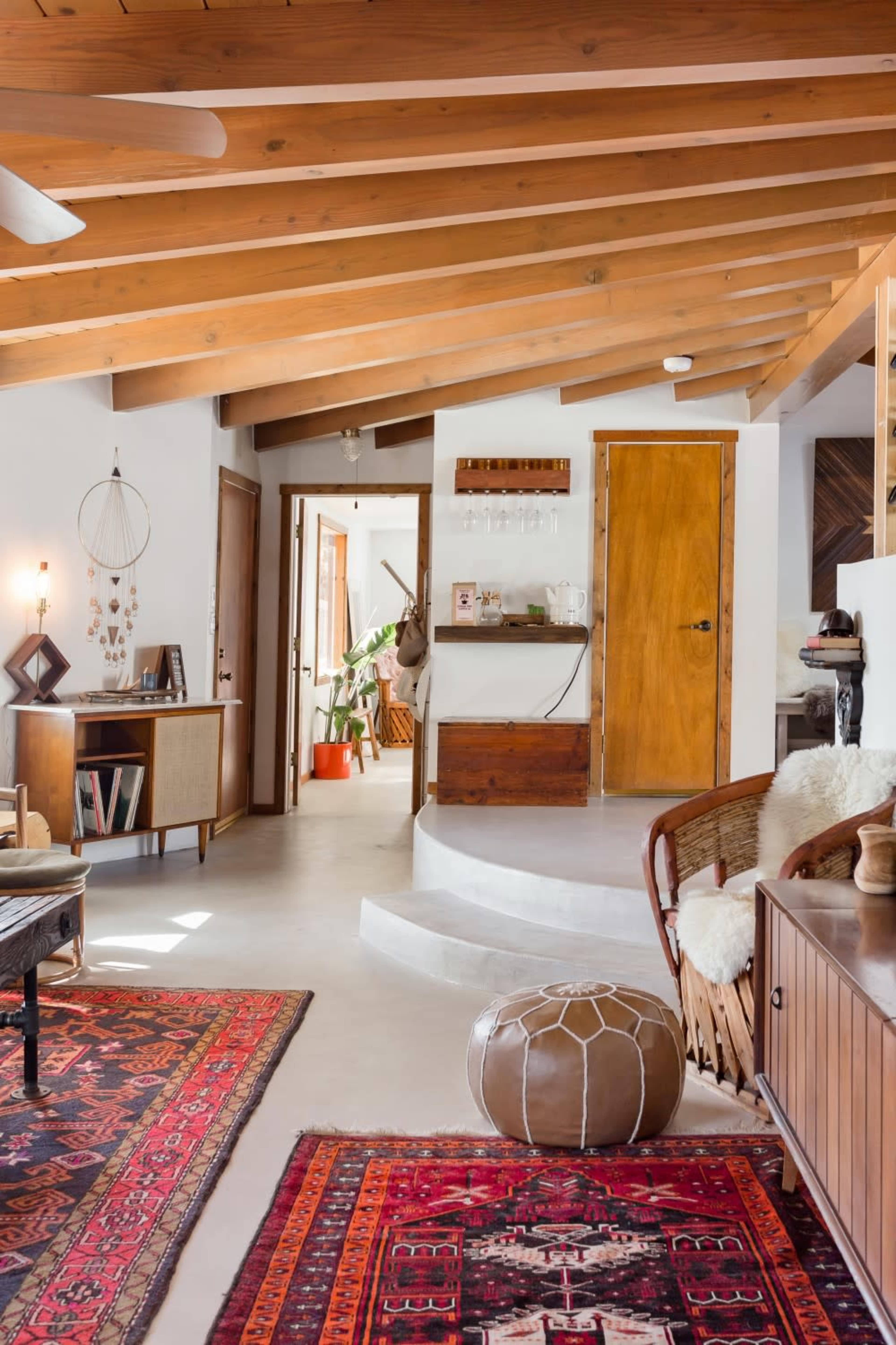 A modern interior space with wooden beams, an open layout, and various rugs on a concrete floor.