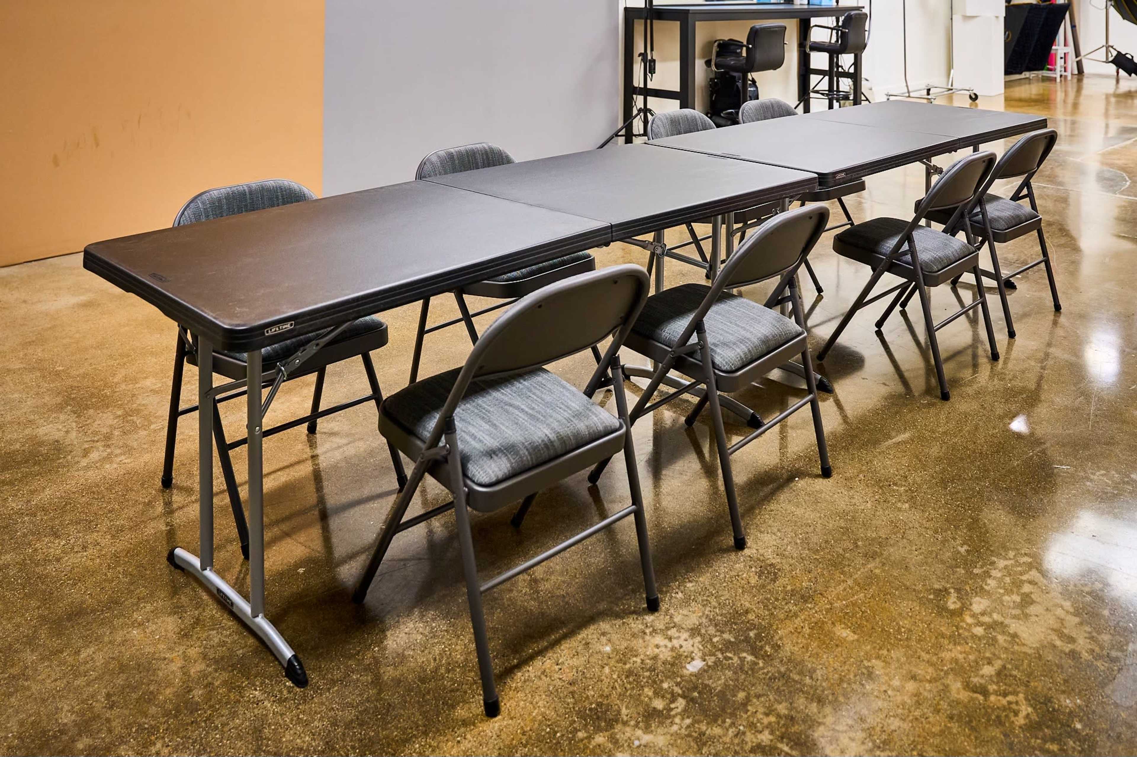 A long folding table is set up with several gray folding chairs around it in a spacious indoor area.