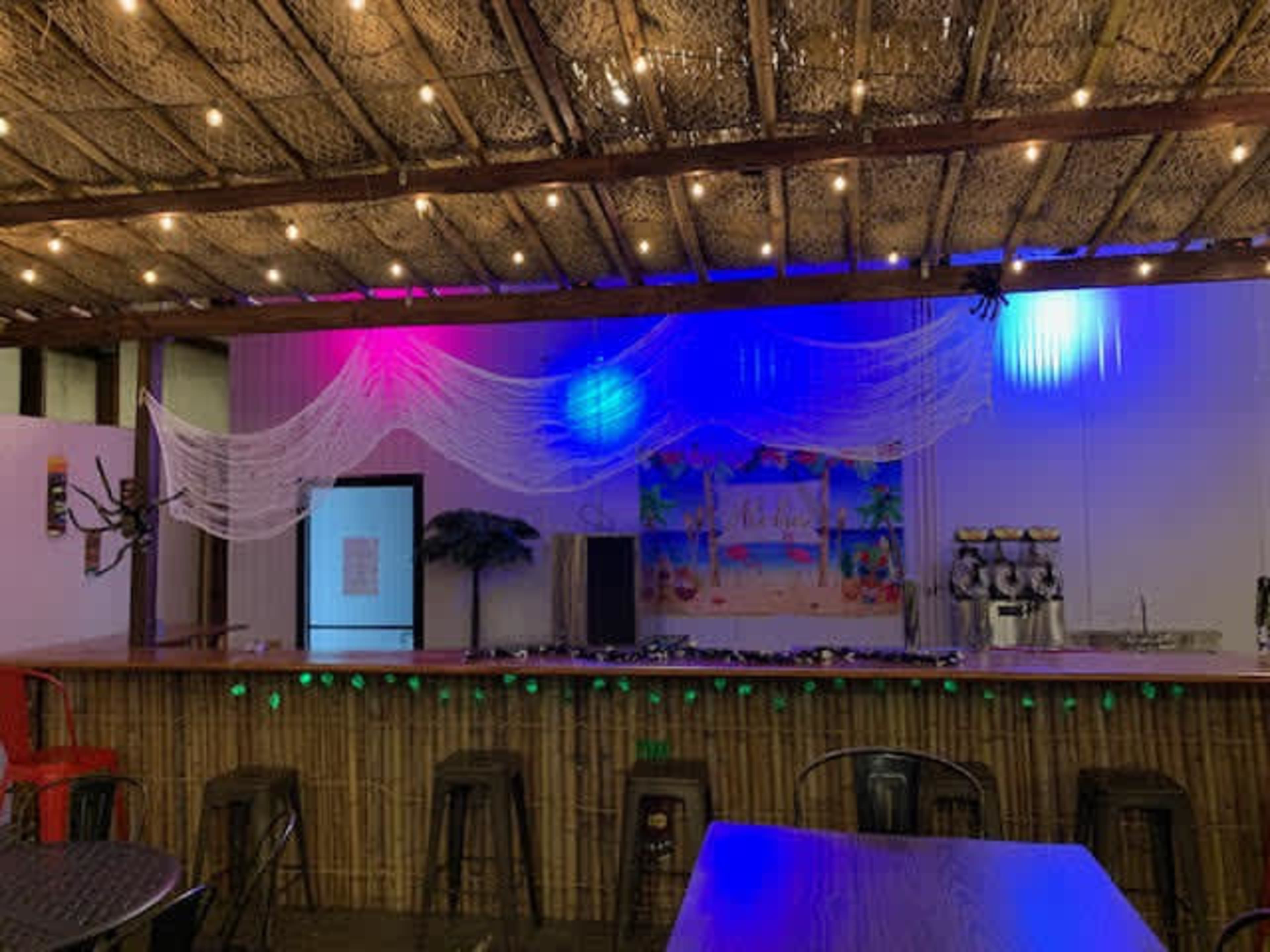 A bar area with a bamboo counter, colorful lights, and decorative netting hanging from the ceiling.