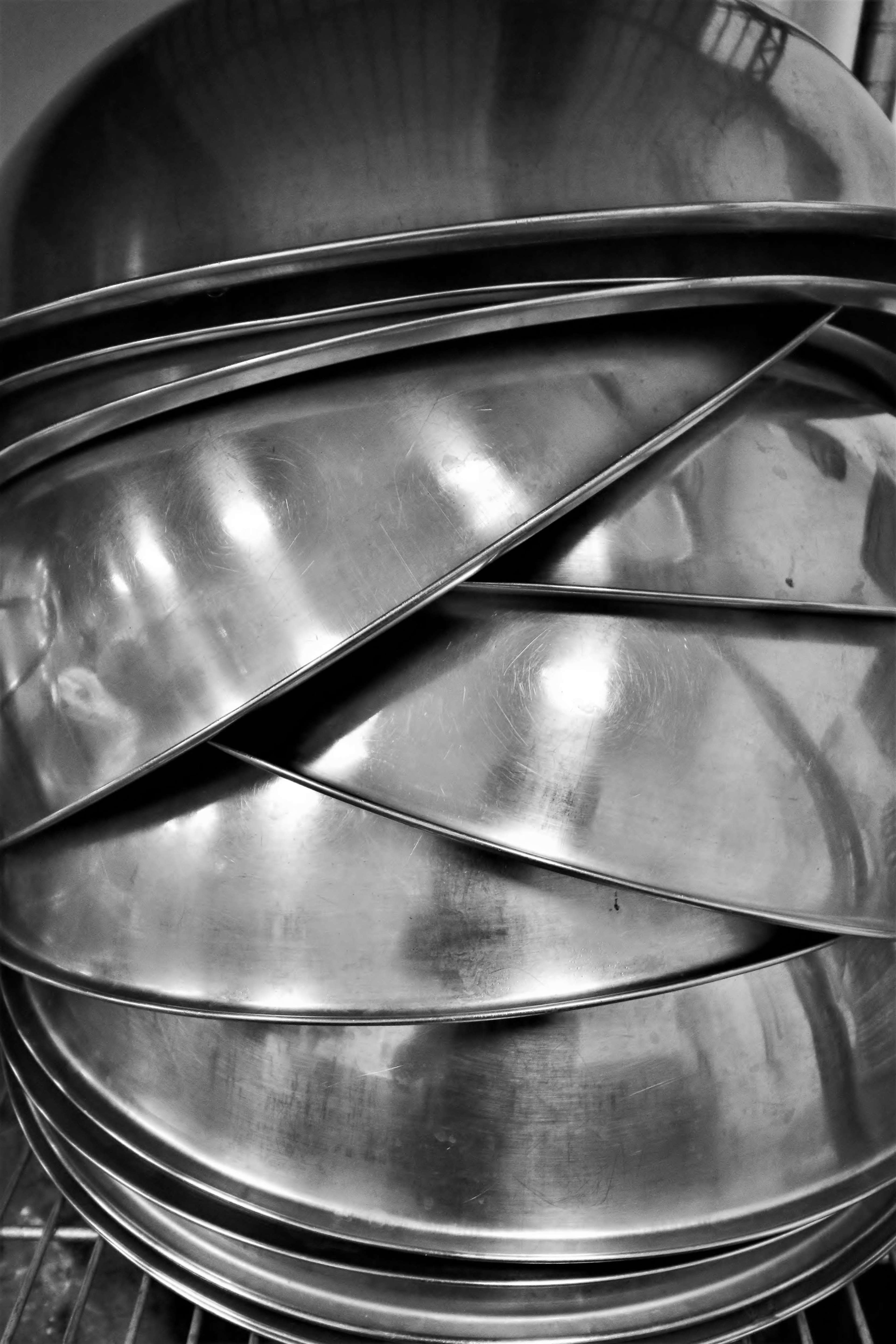 A stack of several shiny metal bowls is arranged in a circular formation on a shelf.