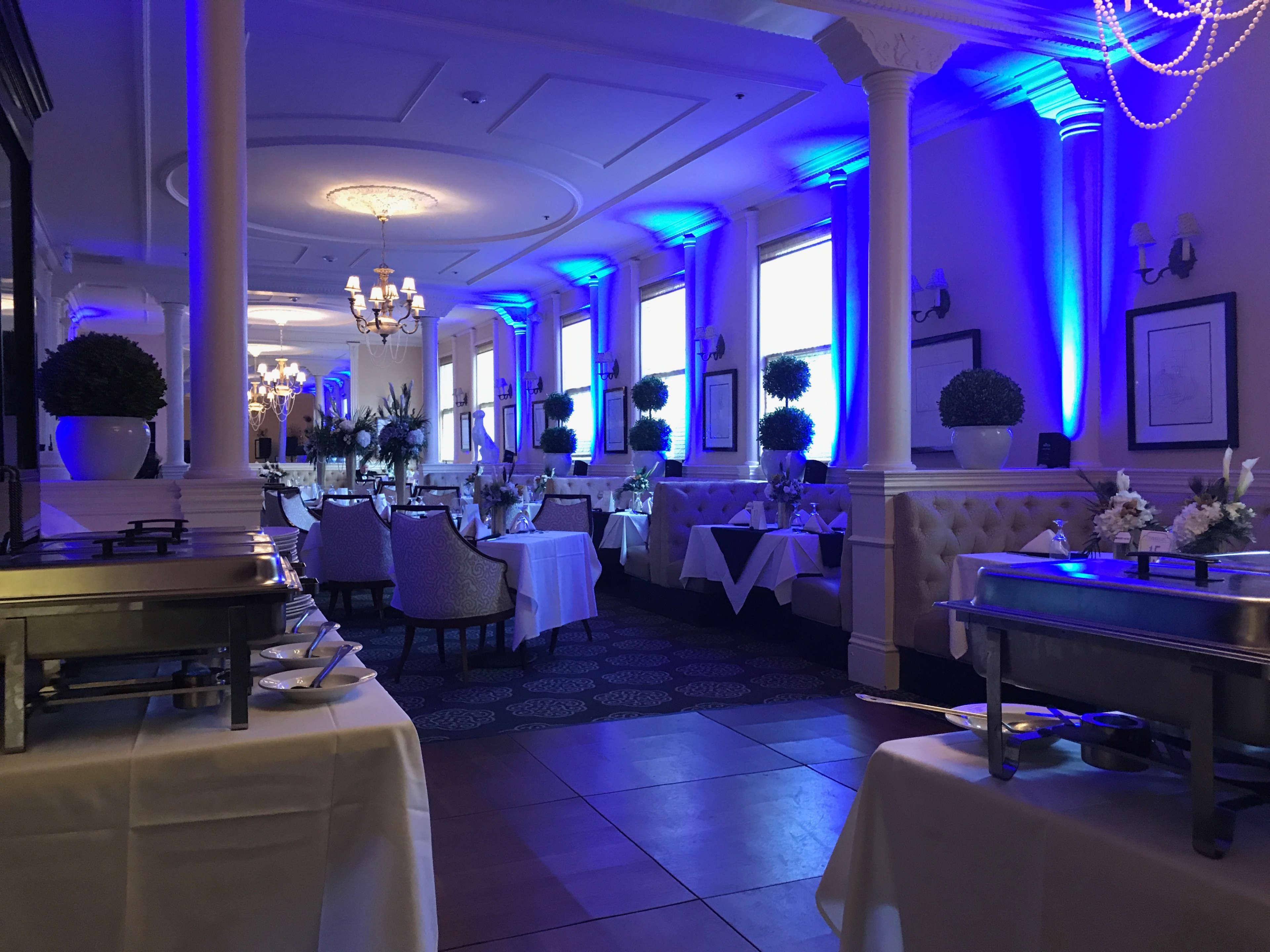A well-lit restaurant featuring white tablecloths, elegant seating, and blue ambient lighting along the walls.