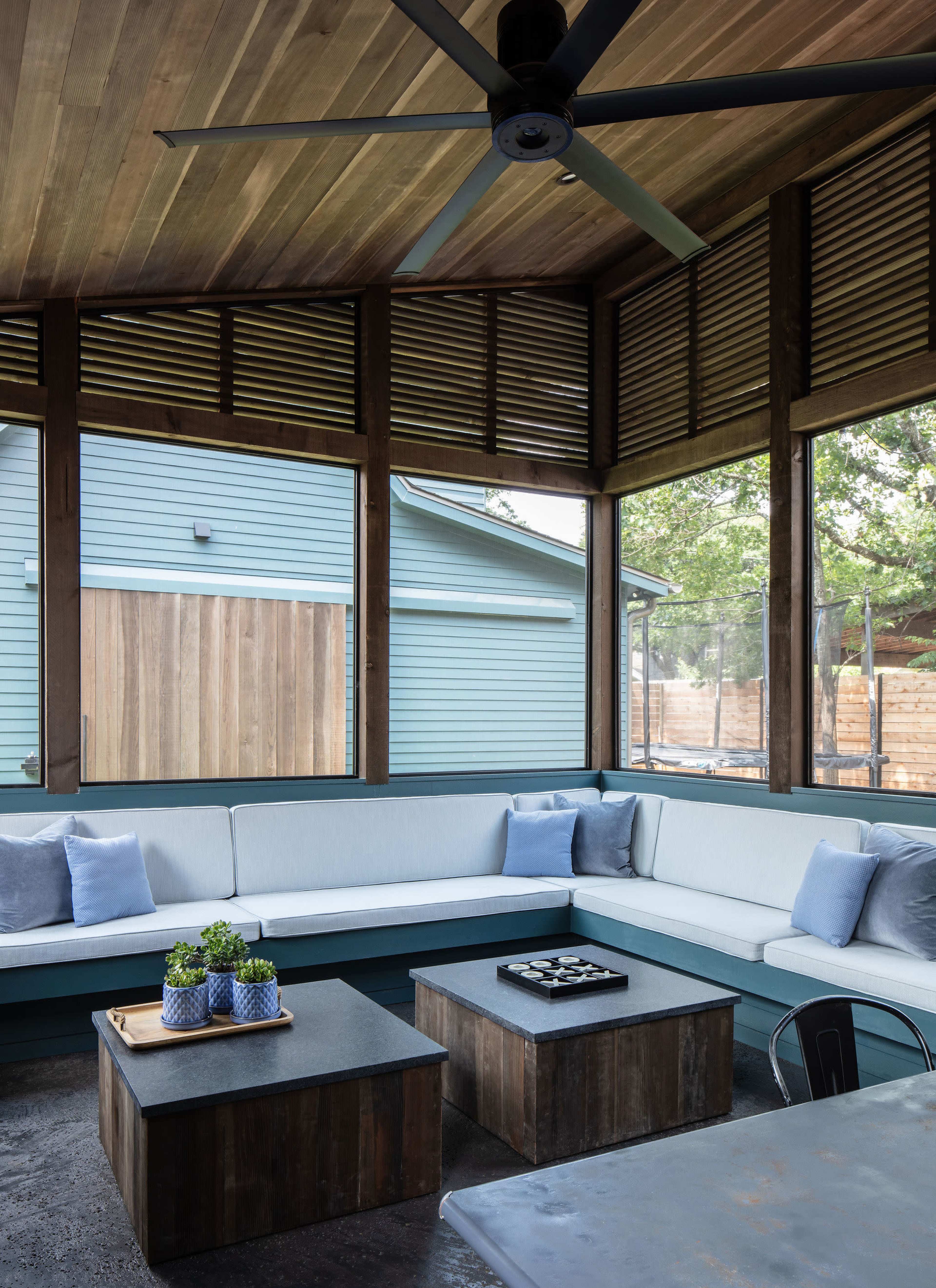 The image shows a screened-in patio with a sectional sofa, two wooden coffee tables, and a ceiling fan.