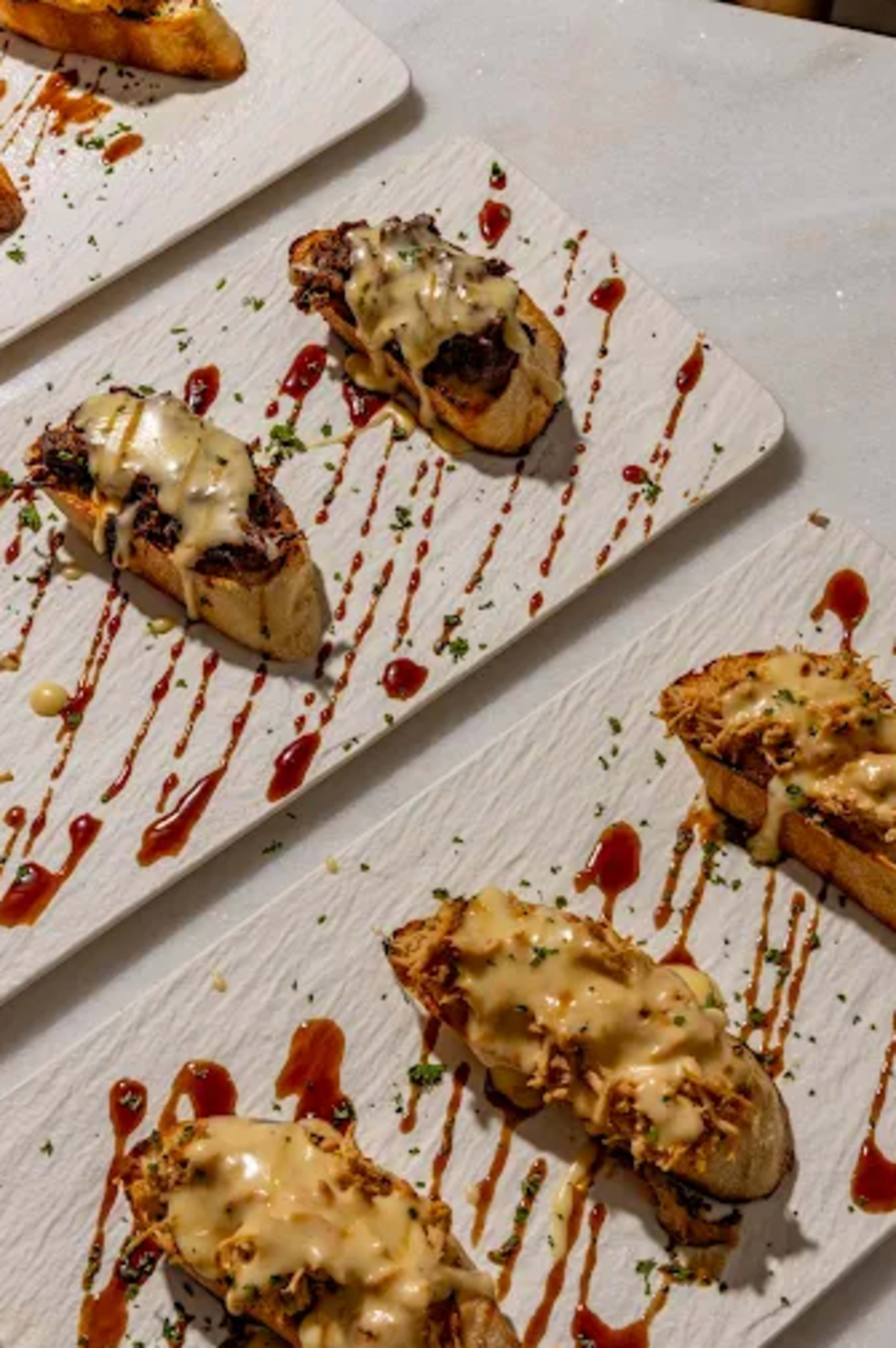 The image shows several pieces of toasted bread topped with a meat mixture and drizzled with sauce on a textured white serving plate.