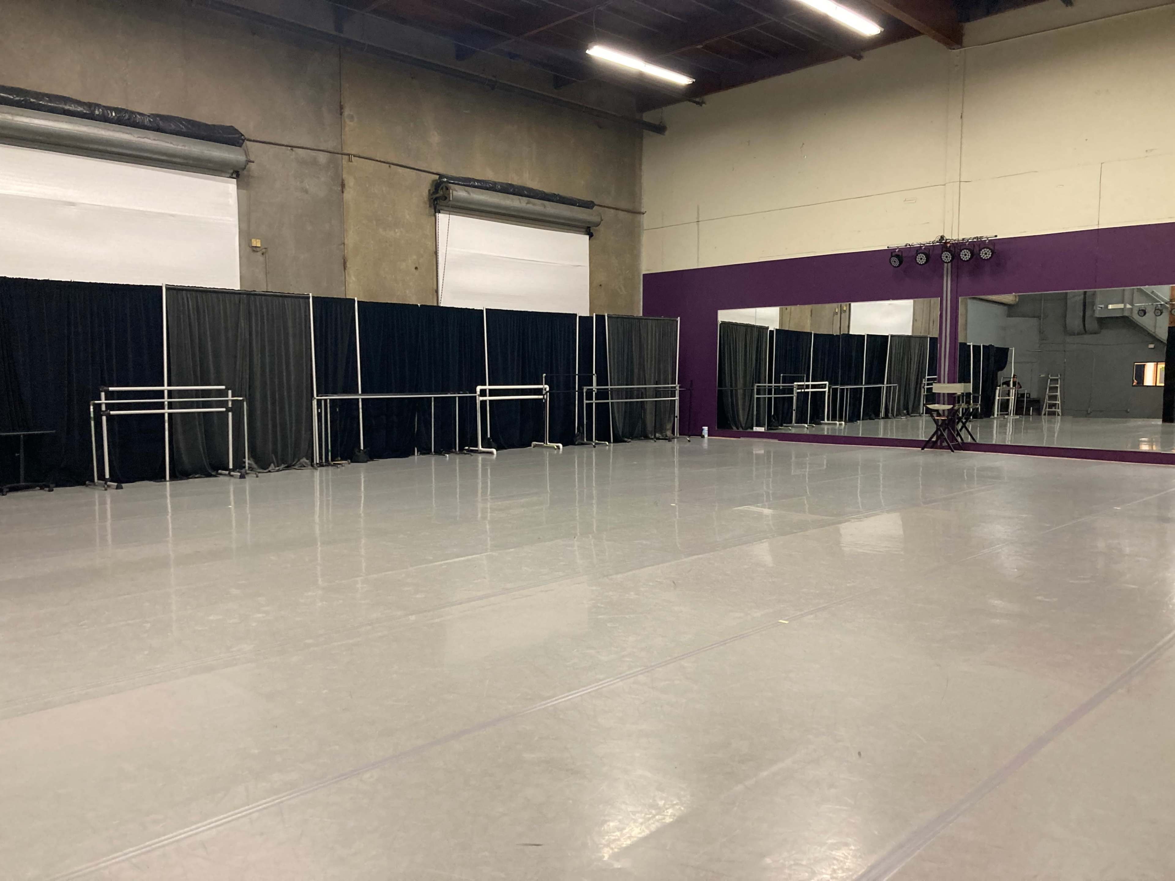 A spacious dance studio with a polished floor, mirrors on one wall, and curtains dividing the area.