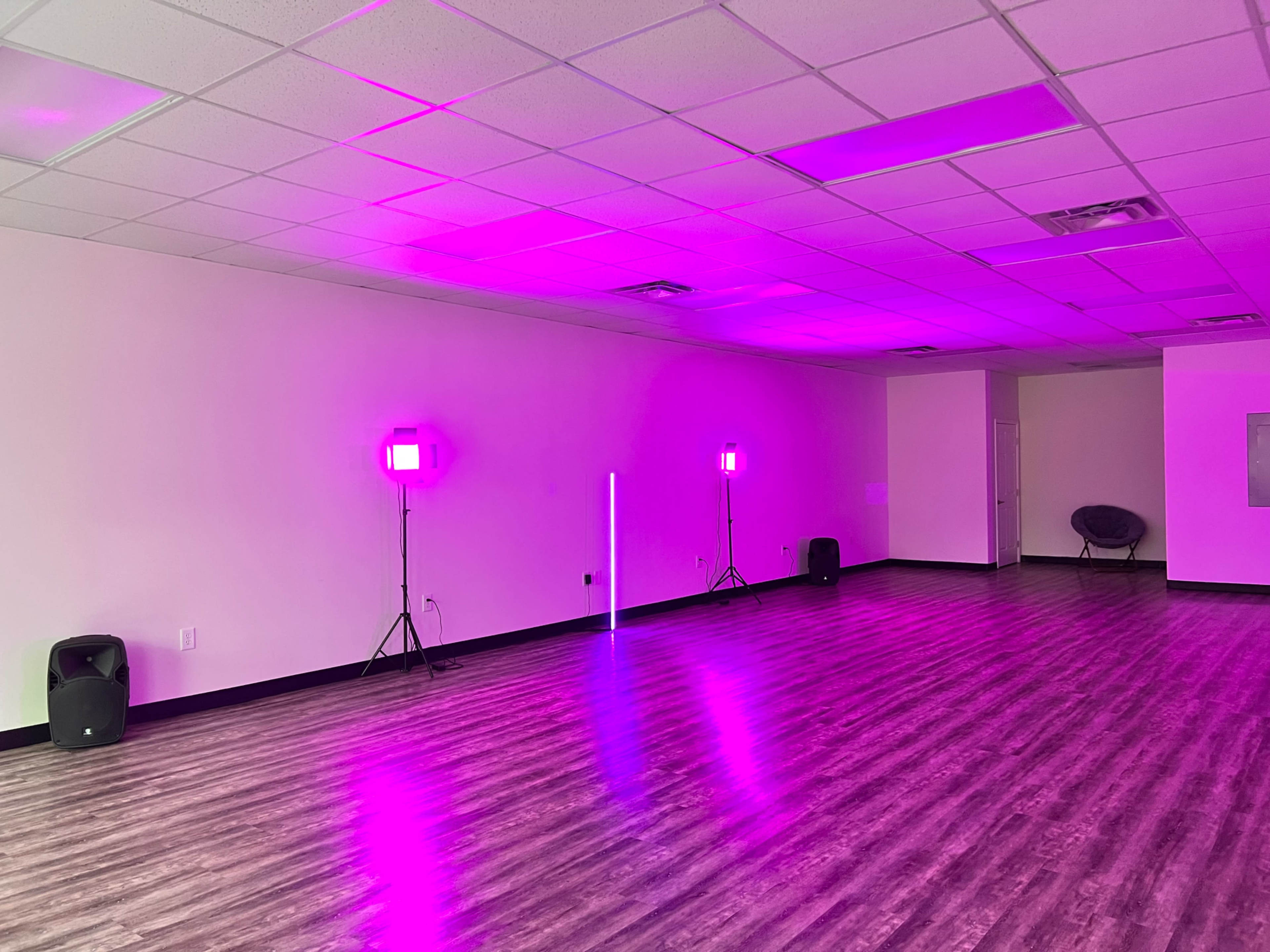 An empty room with purple lighting, featuring two light stands and speakers on the floor.