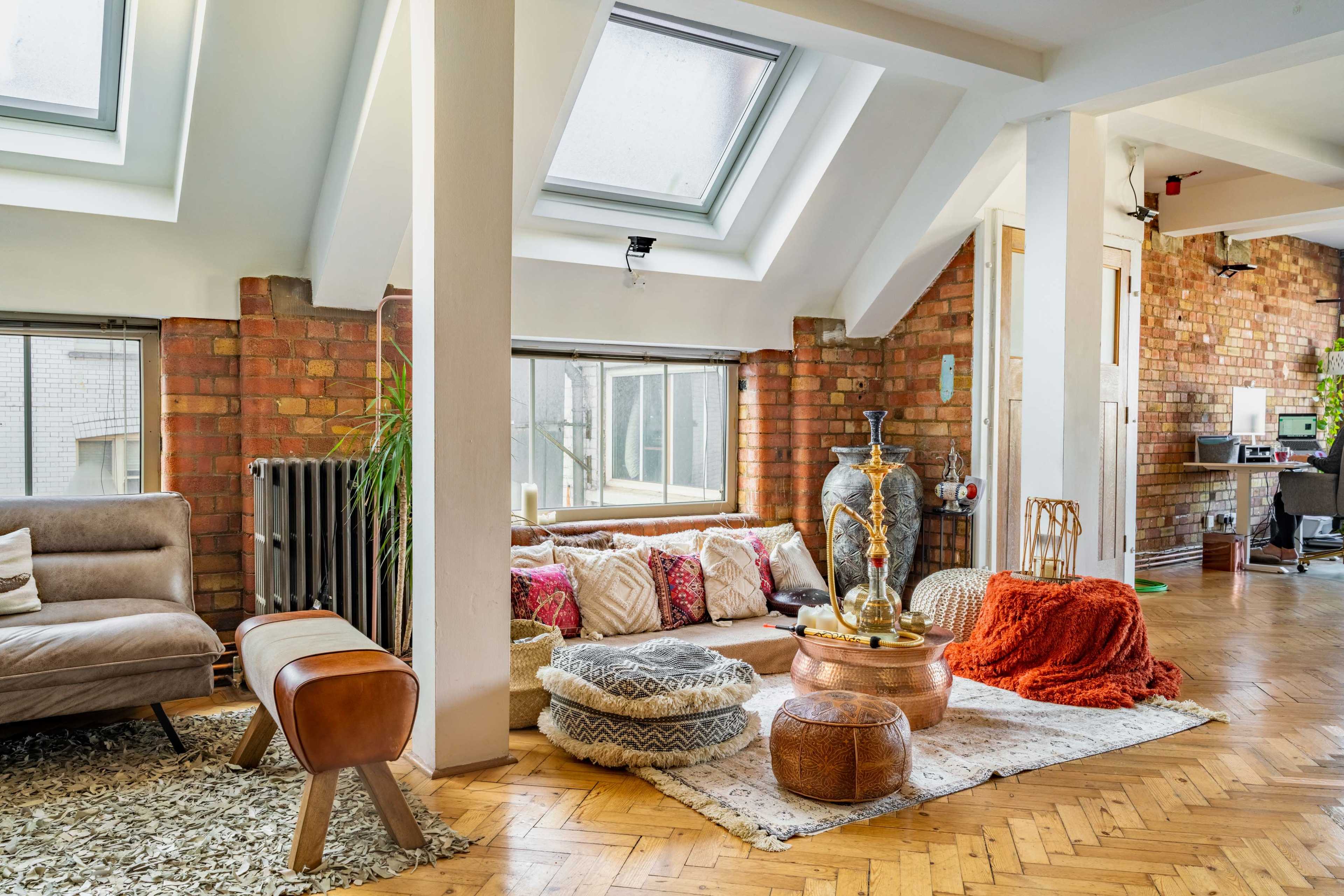 A stylish, open living room with a mix of modern and rustic furnishings, including a sofa, various cushions, a wooden coffee table, and large skylights illuminating the space.