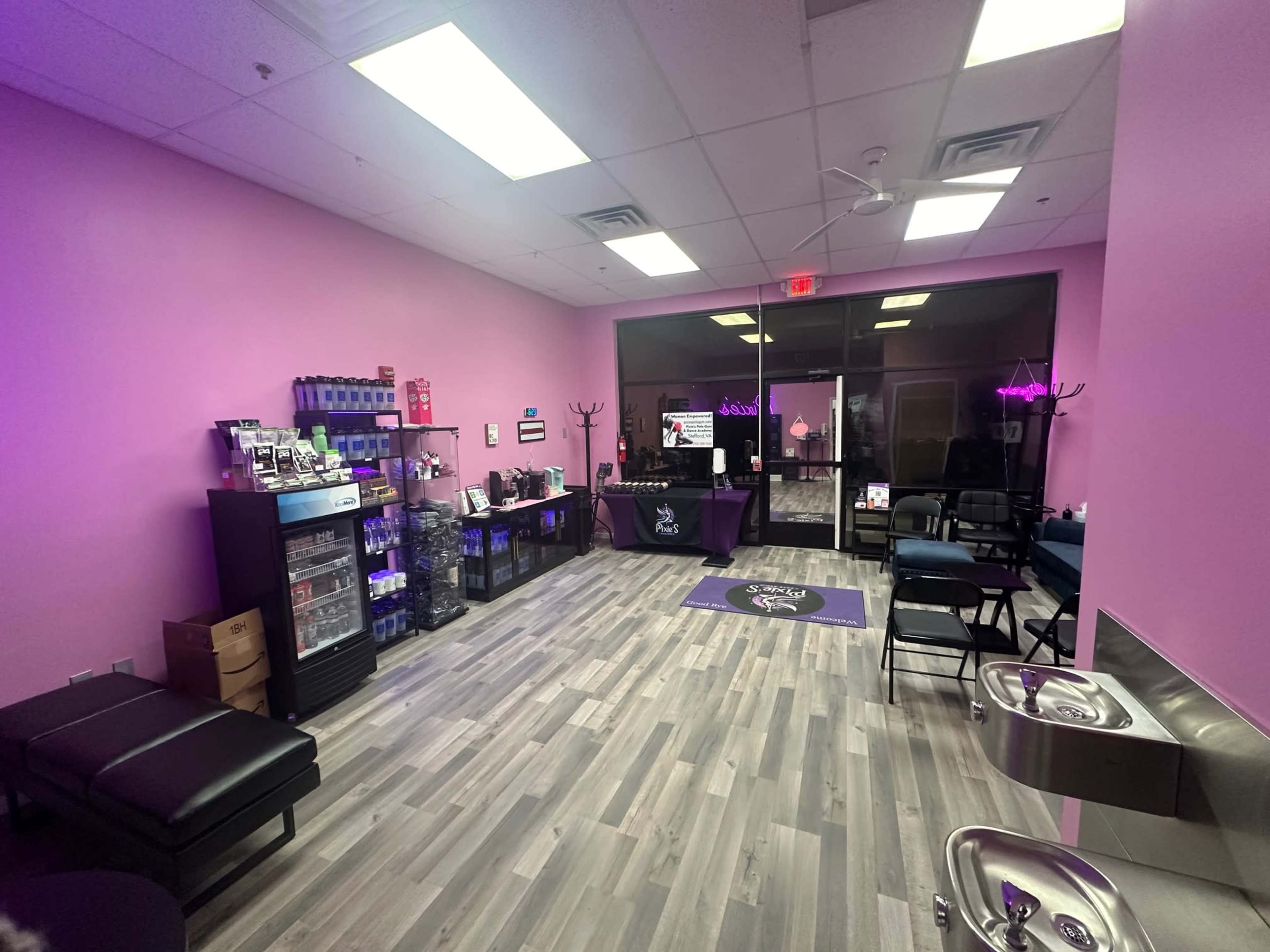 A brightly lit interior of a shop with pink walls, featuring shelves of products, seating areas, and a reception desk at the front.