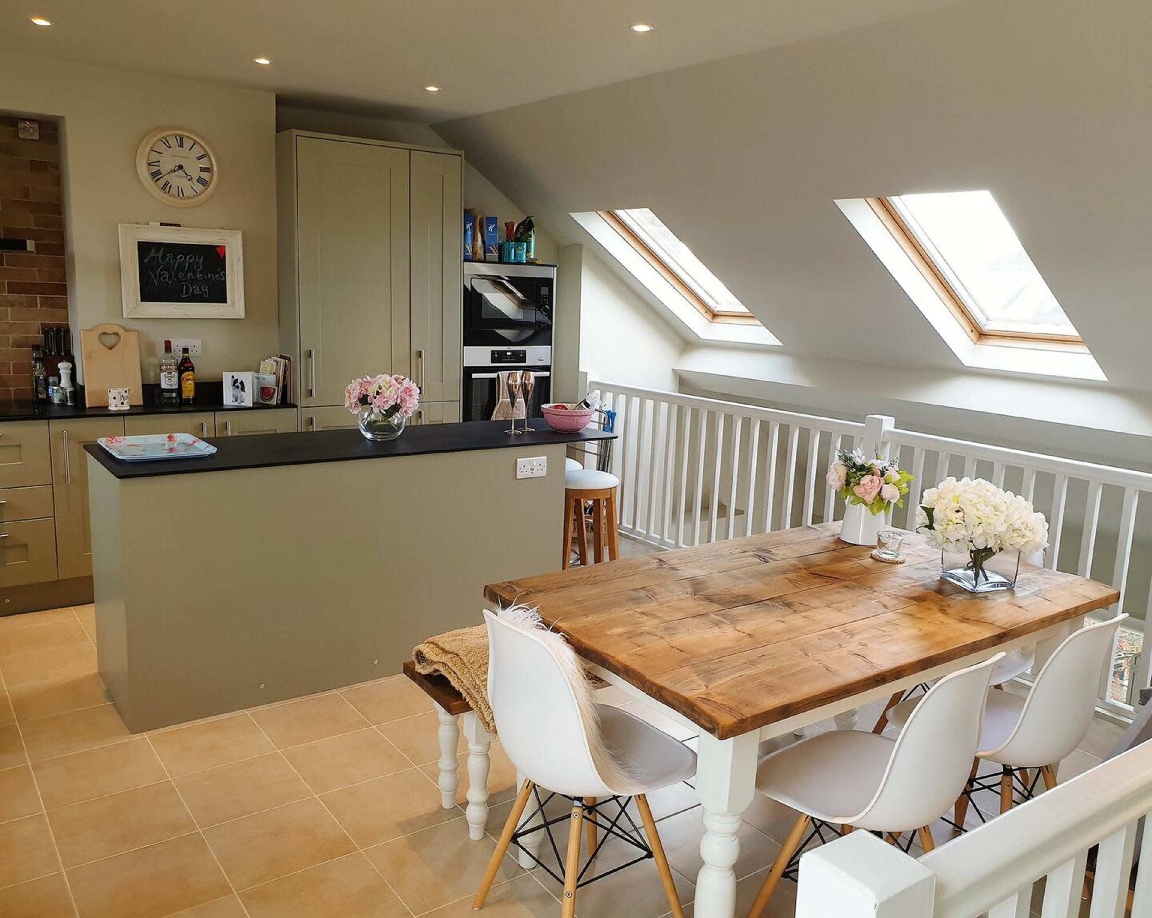 A modern kitchen and dining area features a wooden table with white chairs, skylights, and a well-organized countertop.