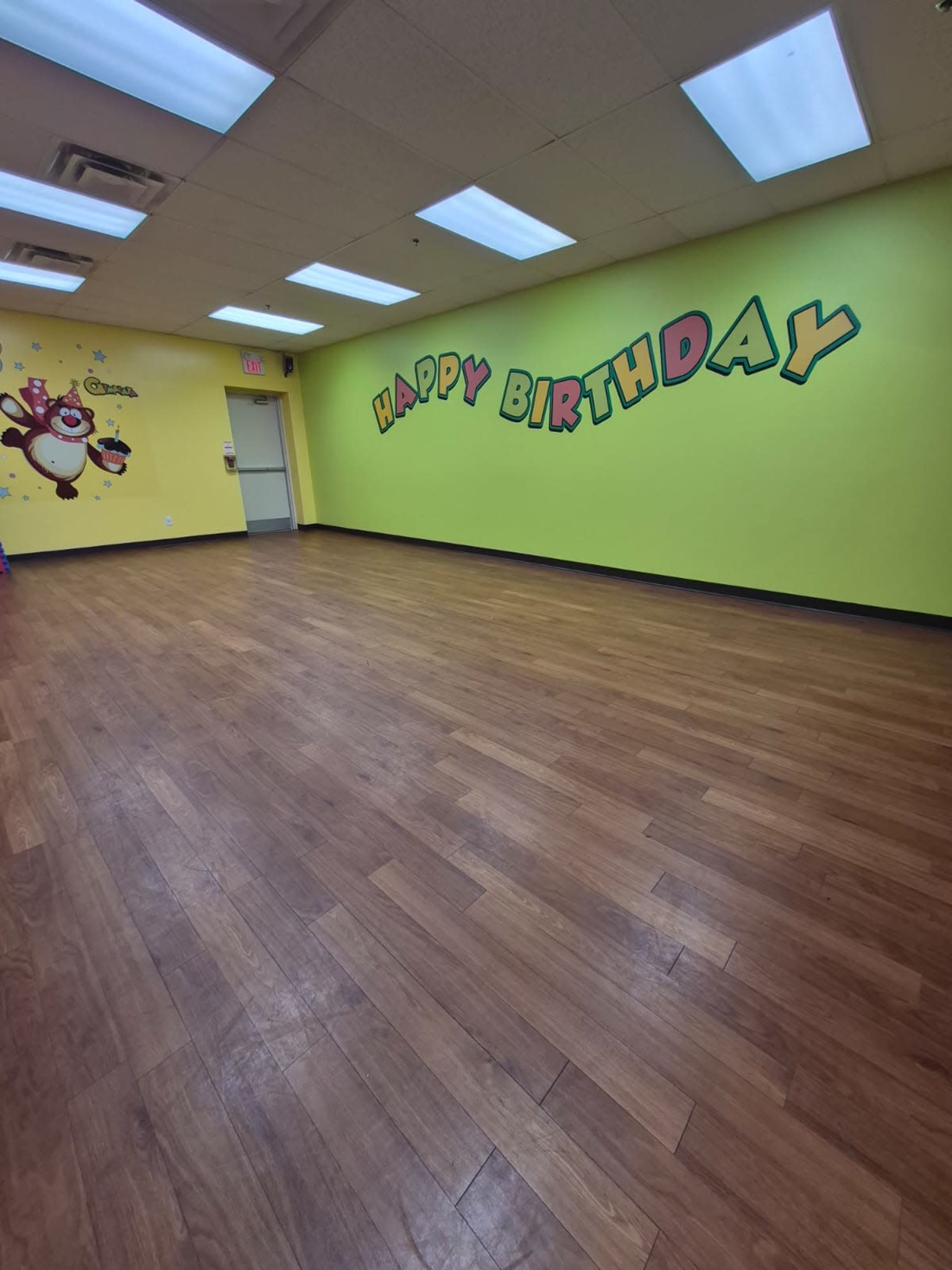 The image shows a brightly colored room with a yellow wall displaying the words "HAPPY BIRTHDAY" and wooden flooring.