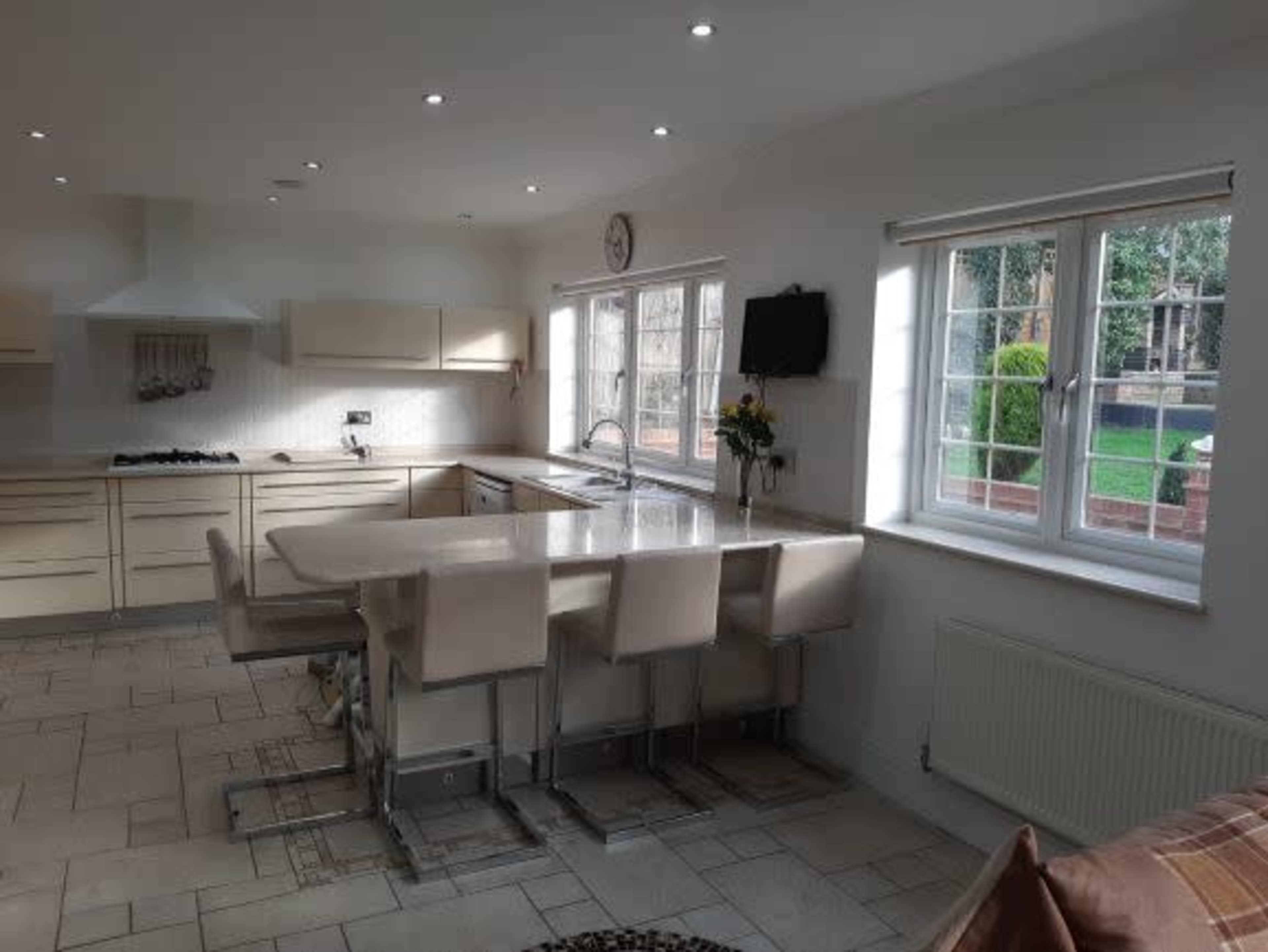 A modern kitchen features a central island with seating, white cabinetry, and large windows overlooking a garden.