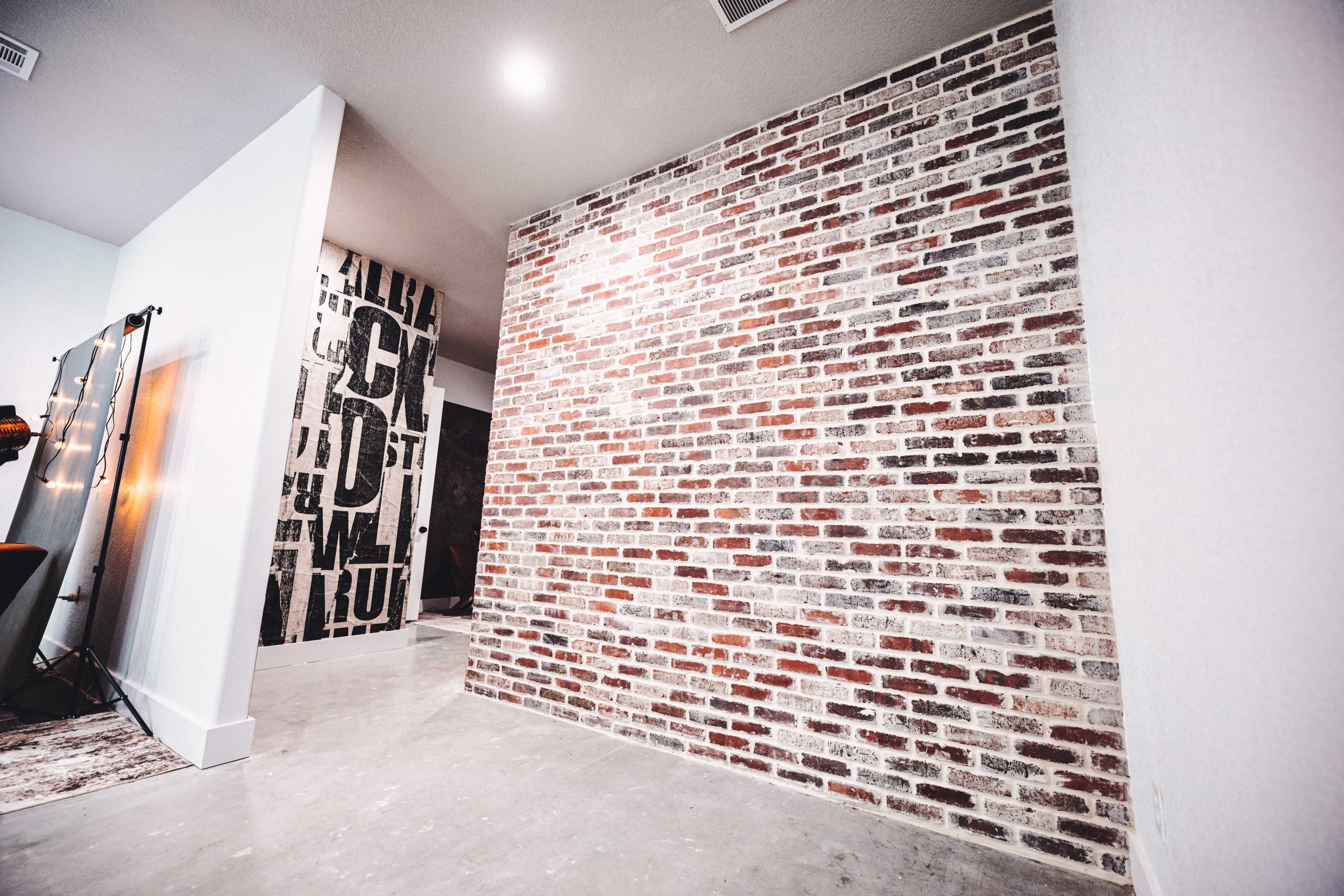 The image shows a modern interior featuring a brick accent wall, concrete flooring, and a partially visible wall with bold black text.