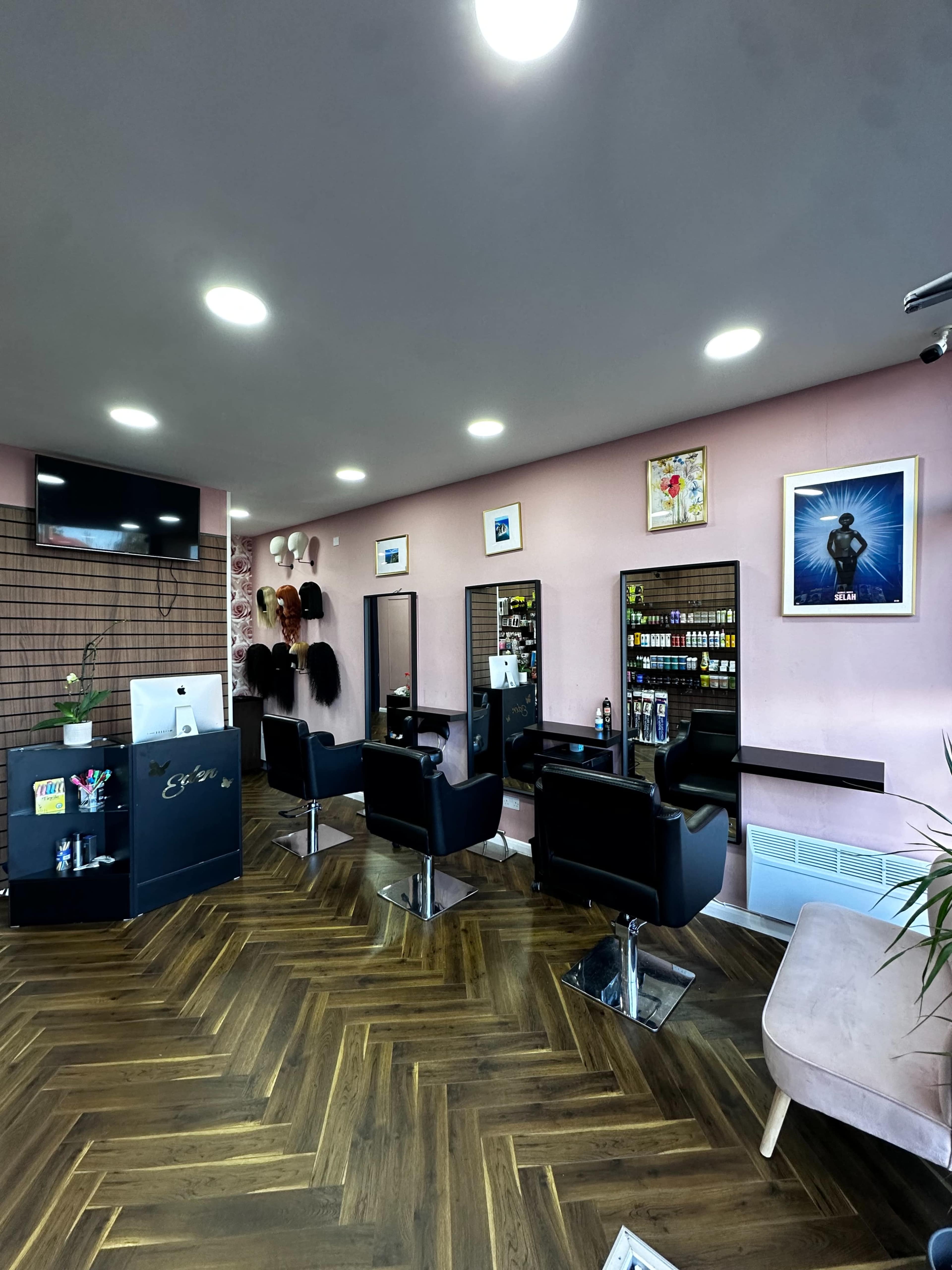 The image shows a modern hair salon with multiple styling stations equipped with mirrors and black chairs, set against pink walls and wooden flooring.
